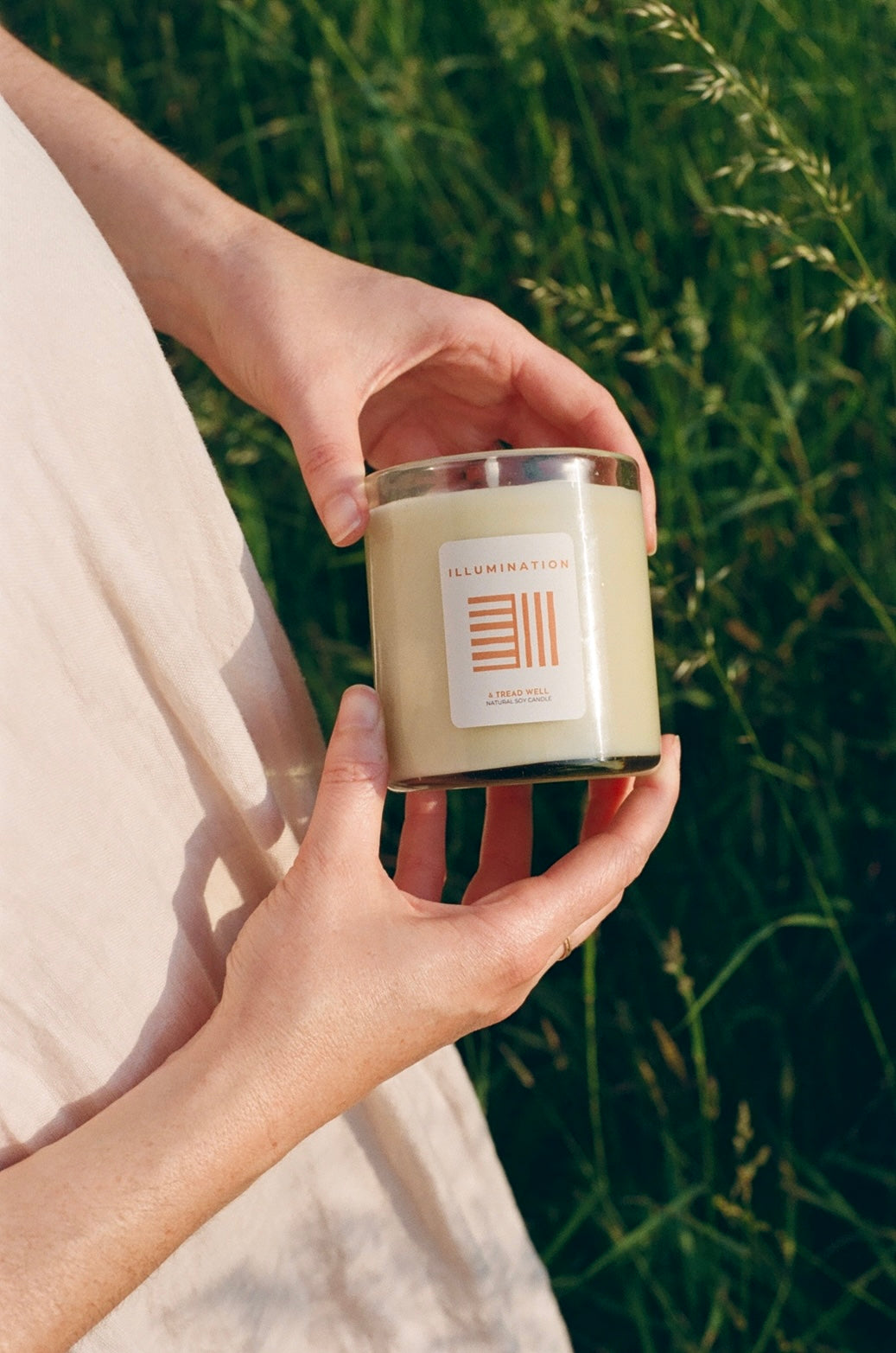 Hand holding a candle labeled 'Harmony' against a natural background
