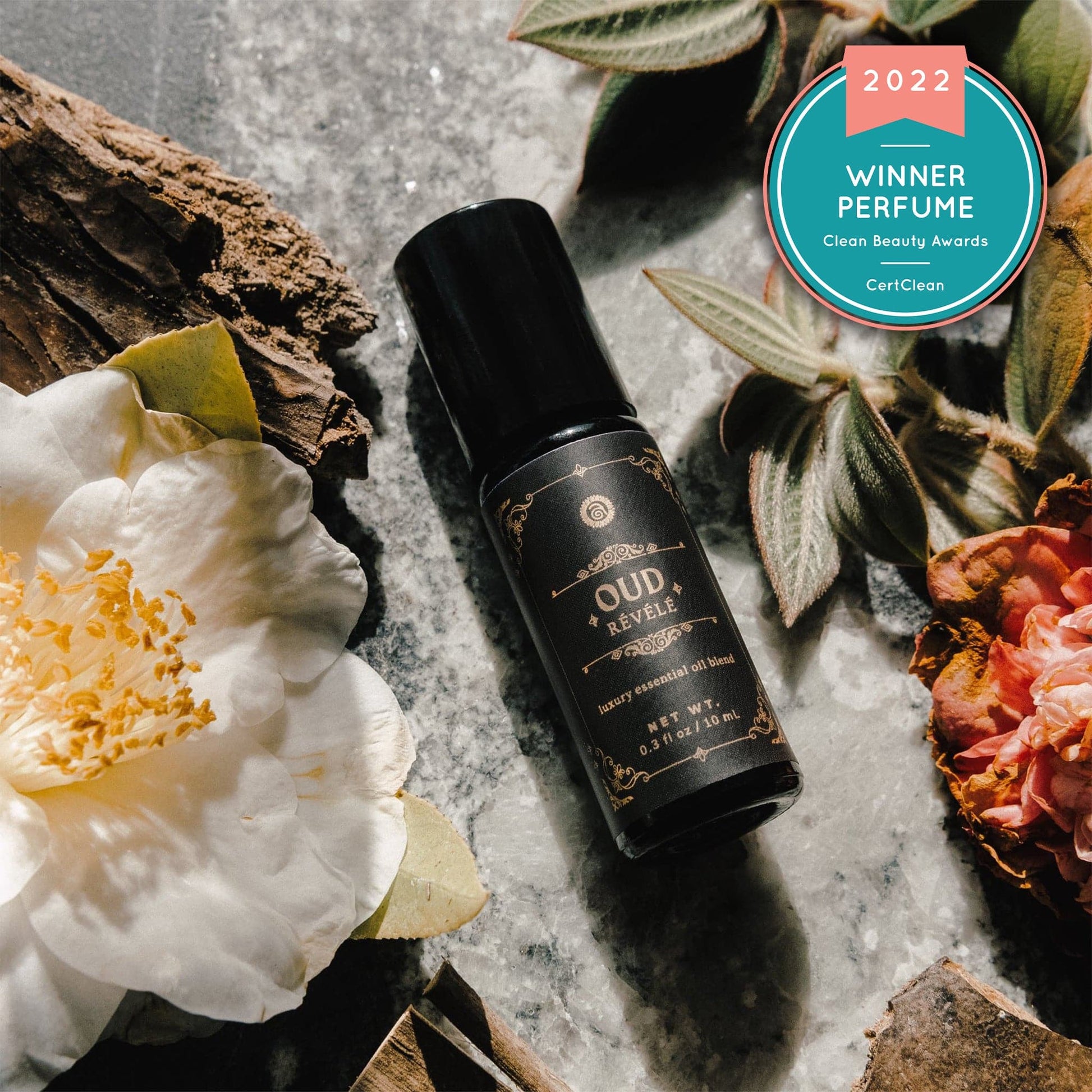 Perfume bottle labeled 'Oud Revele' with flowers and leaves on a textured surface, featuring a 2022 Clean Beauty Award badge.