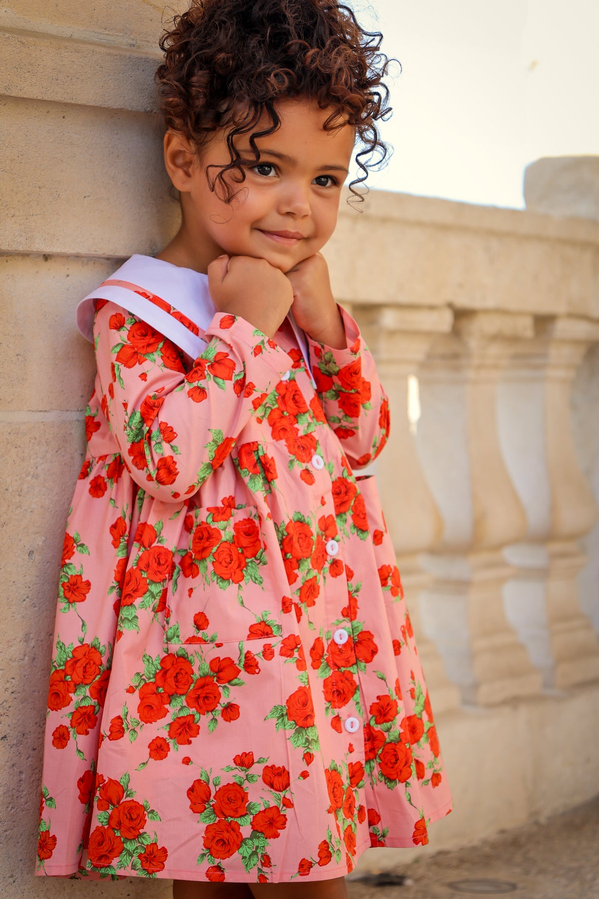 Child wearing a pink floral dress standing against a stone wall.
