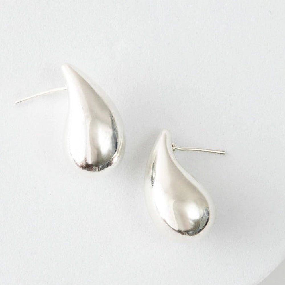 The Dew Drop Studs are mid-sized teardrop studs composed of shiny silver. The teardrop curves slightly, giving the earrings a more natural look.