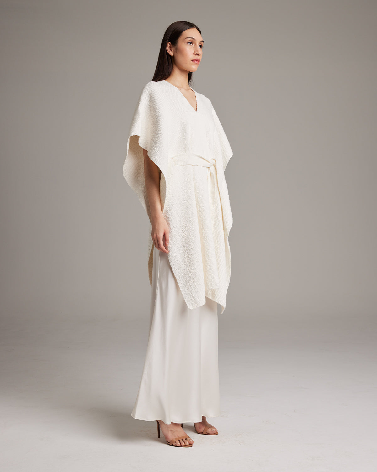 Model wearing a textured white cotton kaftan with a belt, standing against a neutral background.