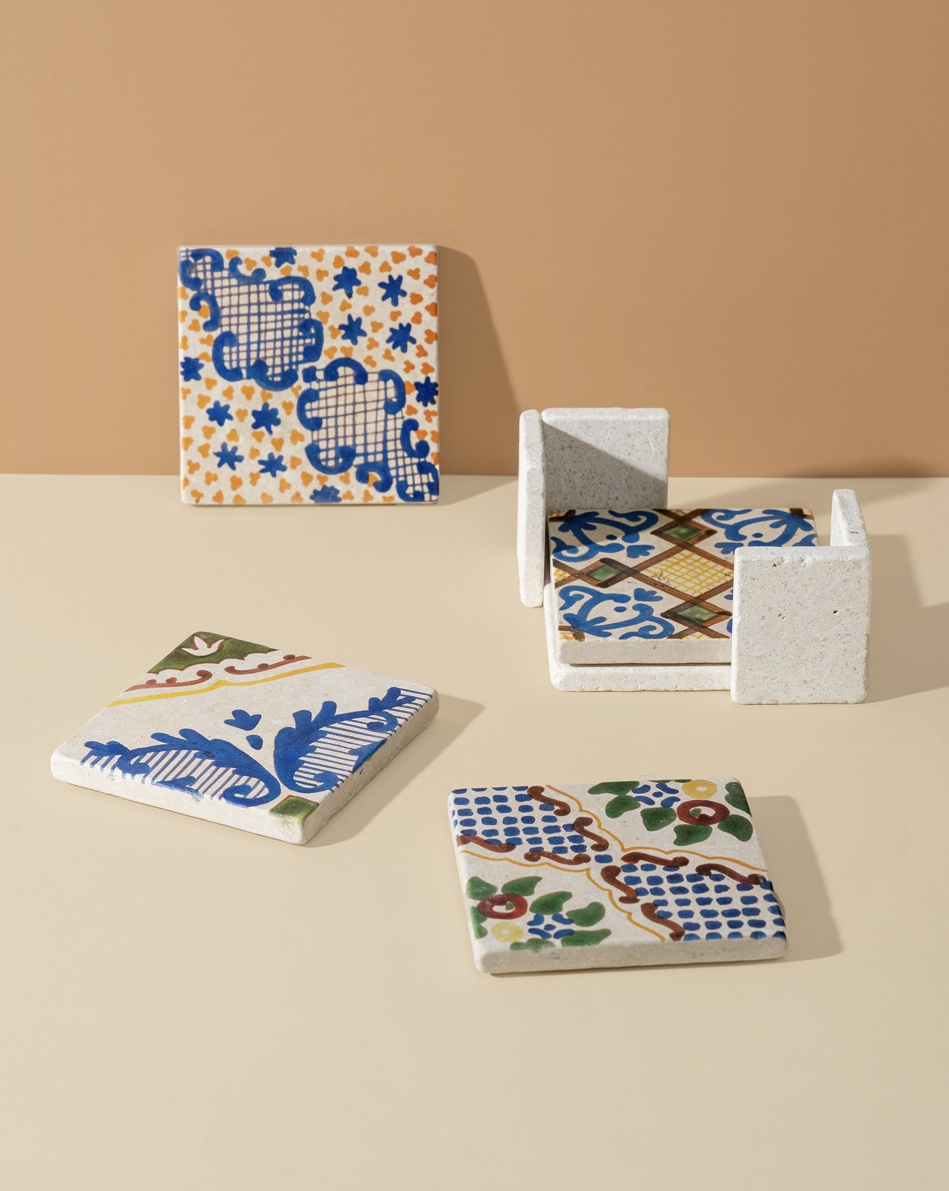 A set of four square marble coasters with hand-finished white and blue patterns, displayed on a neutral background.