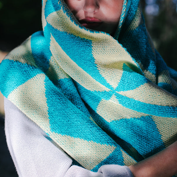 Person wearing a blue and aqua patterned throw blanket around their head like a scarf.