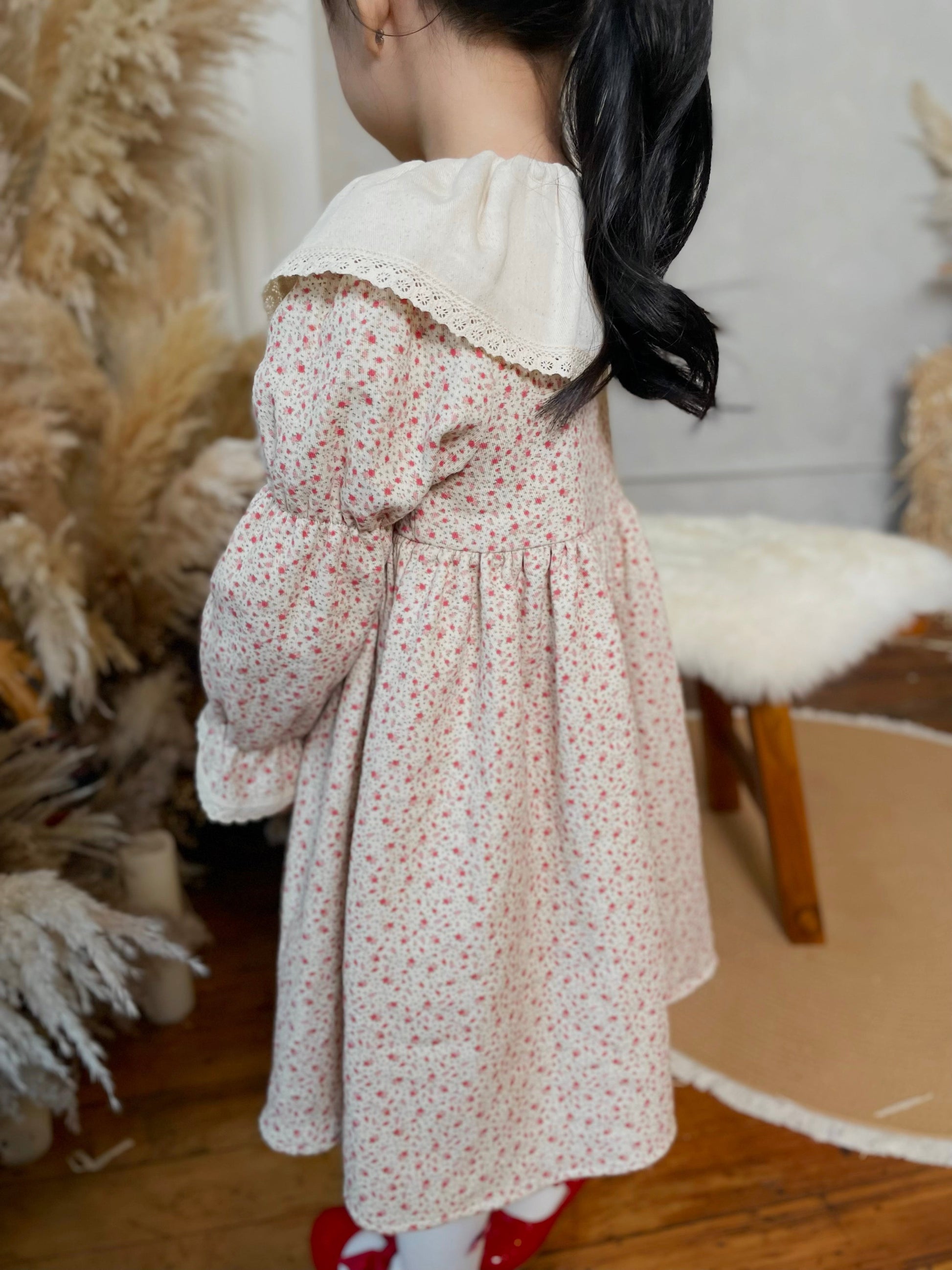 Child wearing a floral dress with a white collar in a home setting