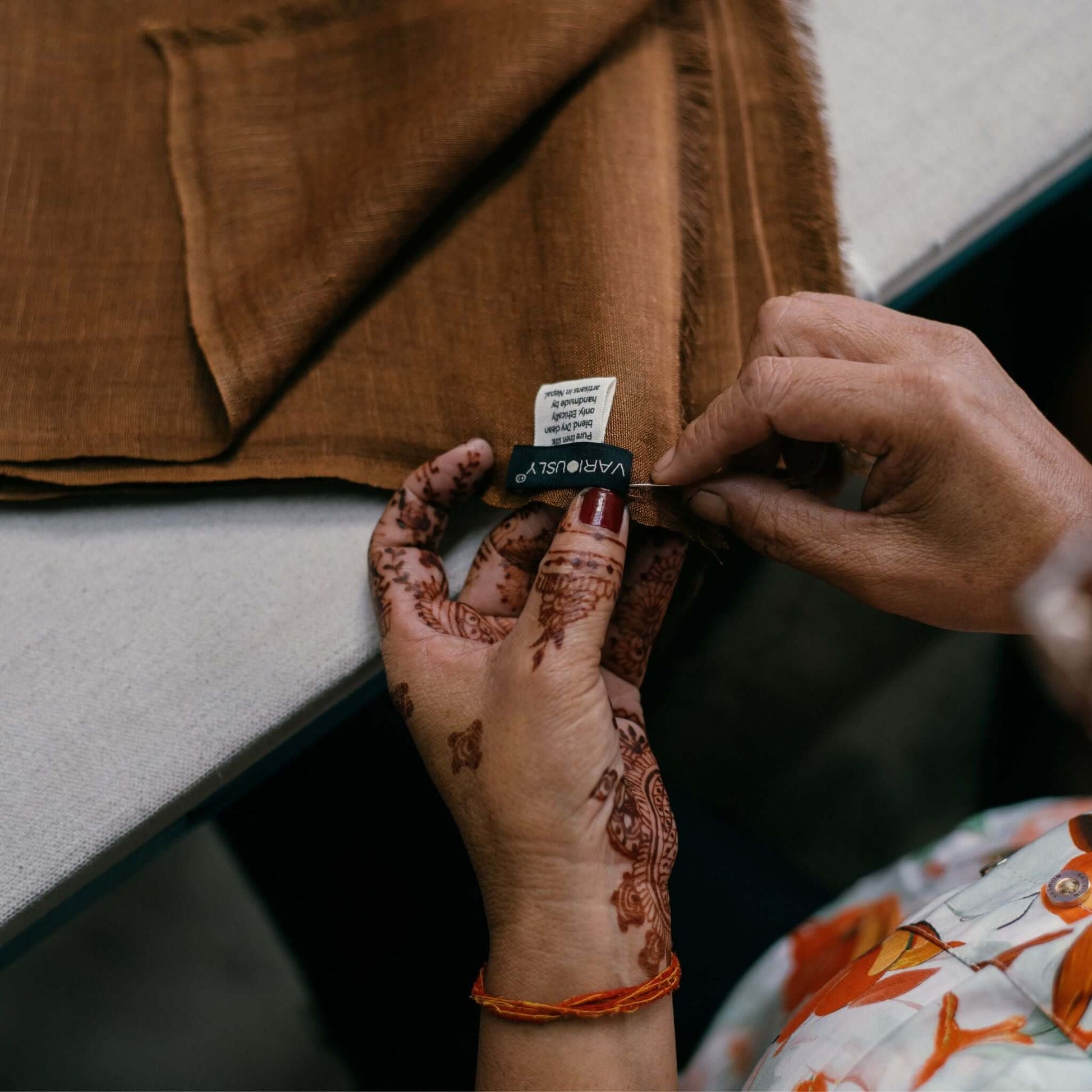Hands examining the label of a Coco Brown Hand Woven Linen Silk Blend Scarf, showcasing artisan craftsmanship.