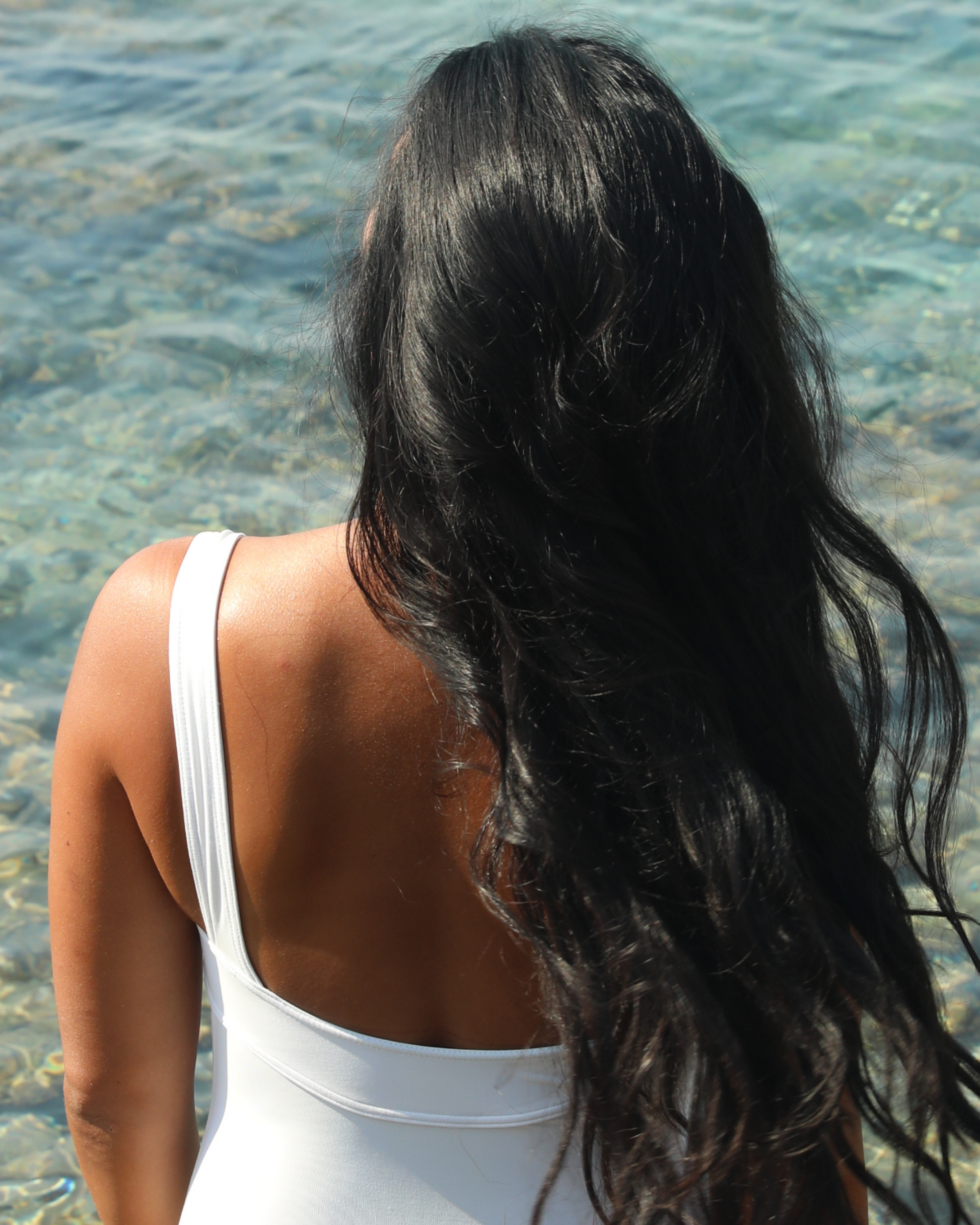 Person with long dark hair standing by a body of water|variant:42-oz