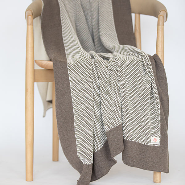 Dark brown and beige patterned throw blanket draped over a wooden chair on a white background.