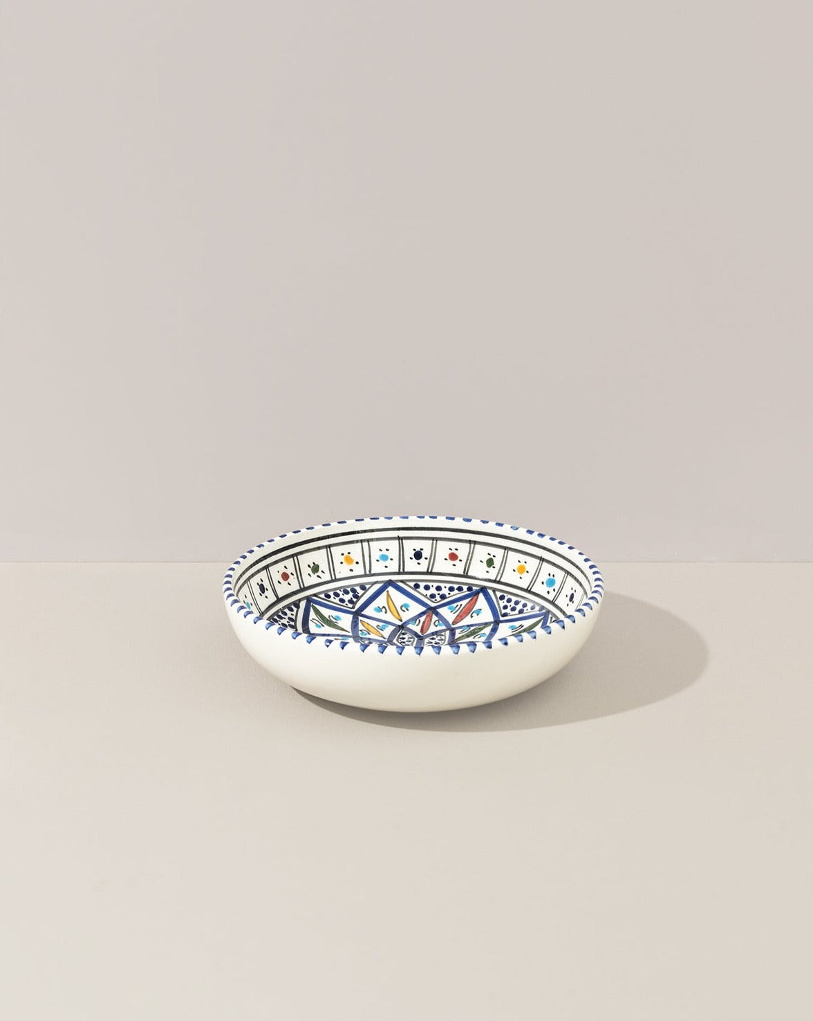 A ceramic hand painted decorative plate with a geometric pattern, predominantly white with blue and gold accents.