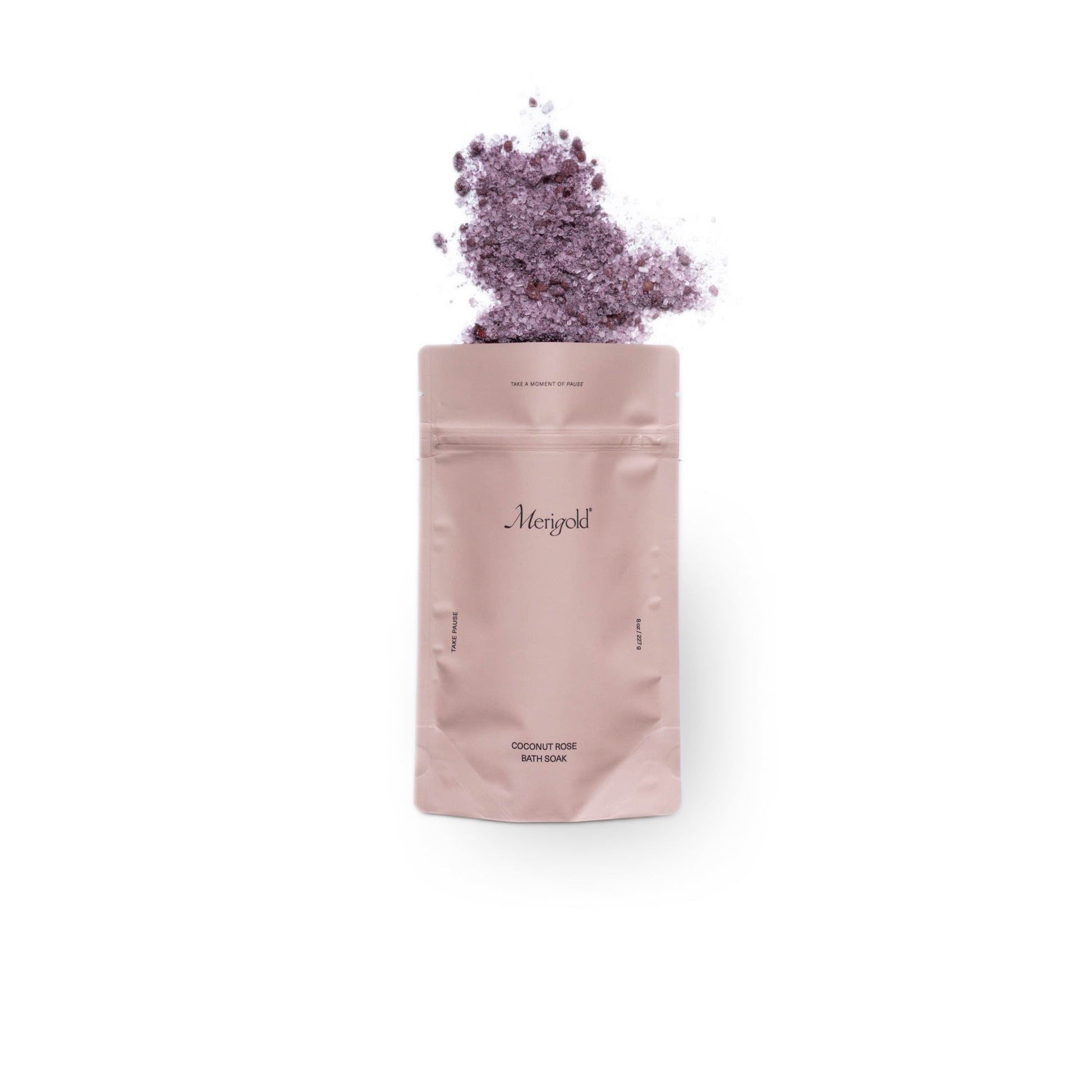 Rose colored bag of Merigold with dried flowers and salts spilling out on a white background.