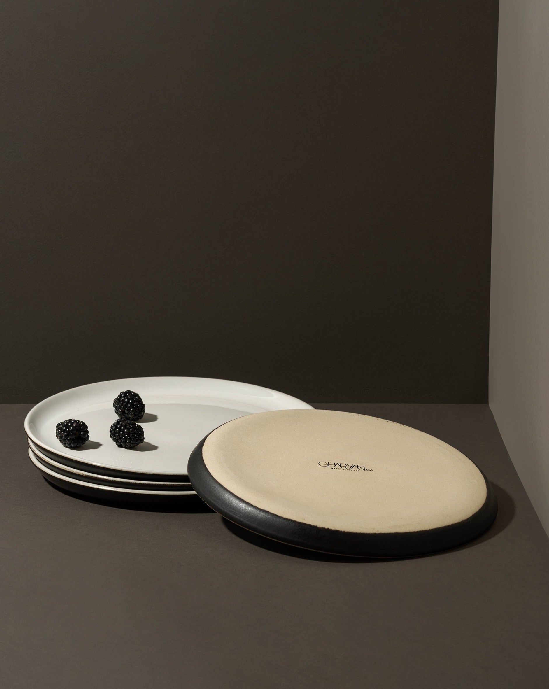 Two stoneware flat plates with a matte finish, one with a plain beige surface and the other with a beige edge and white interior.