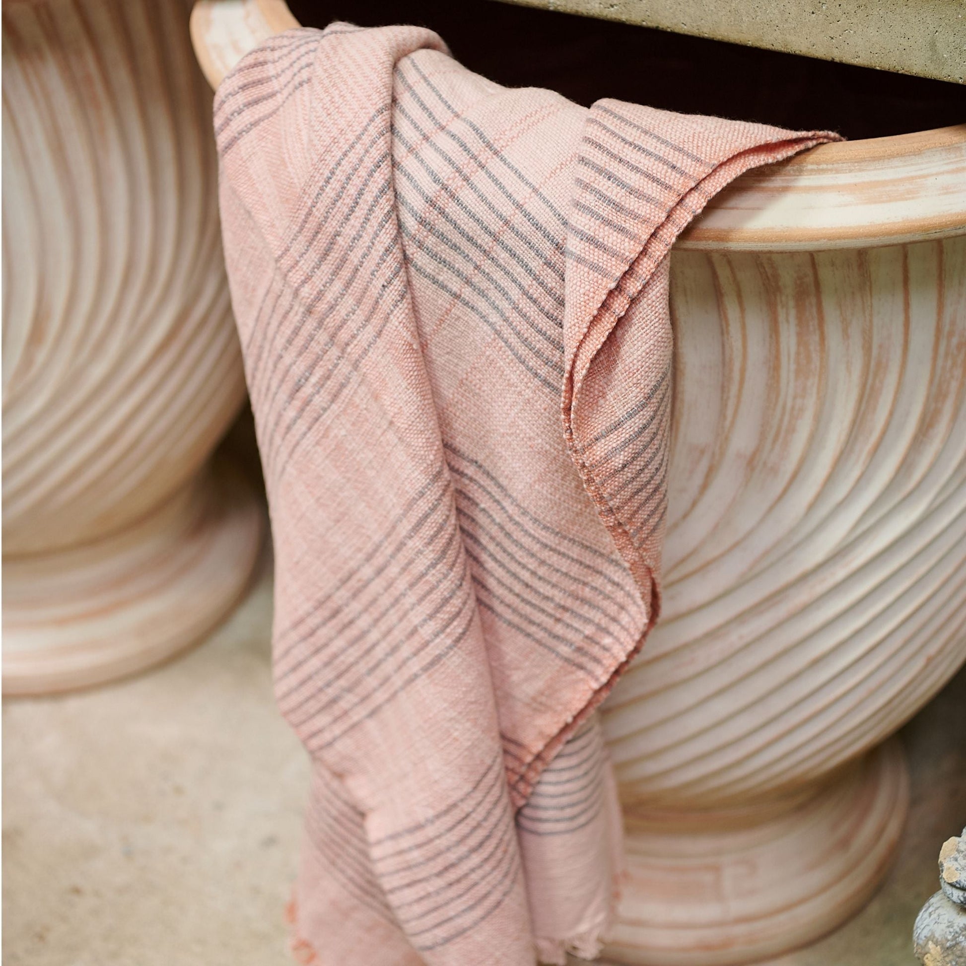 Silica Rose In Shades of Salmon Pink Gray Stripes Pattern Soft Handwoven Merino Throw draped over a decorative pot