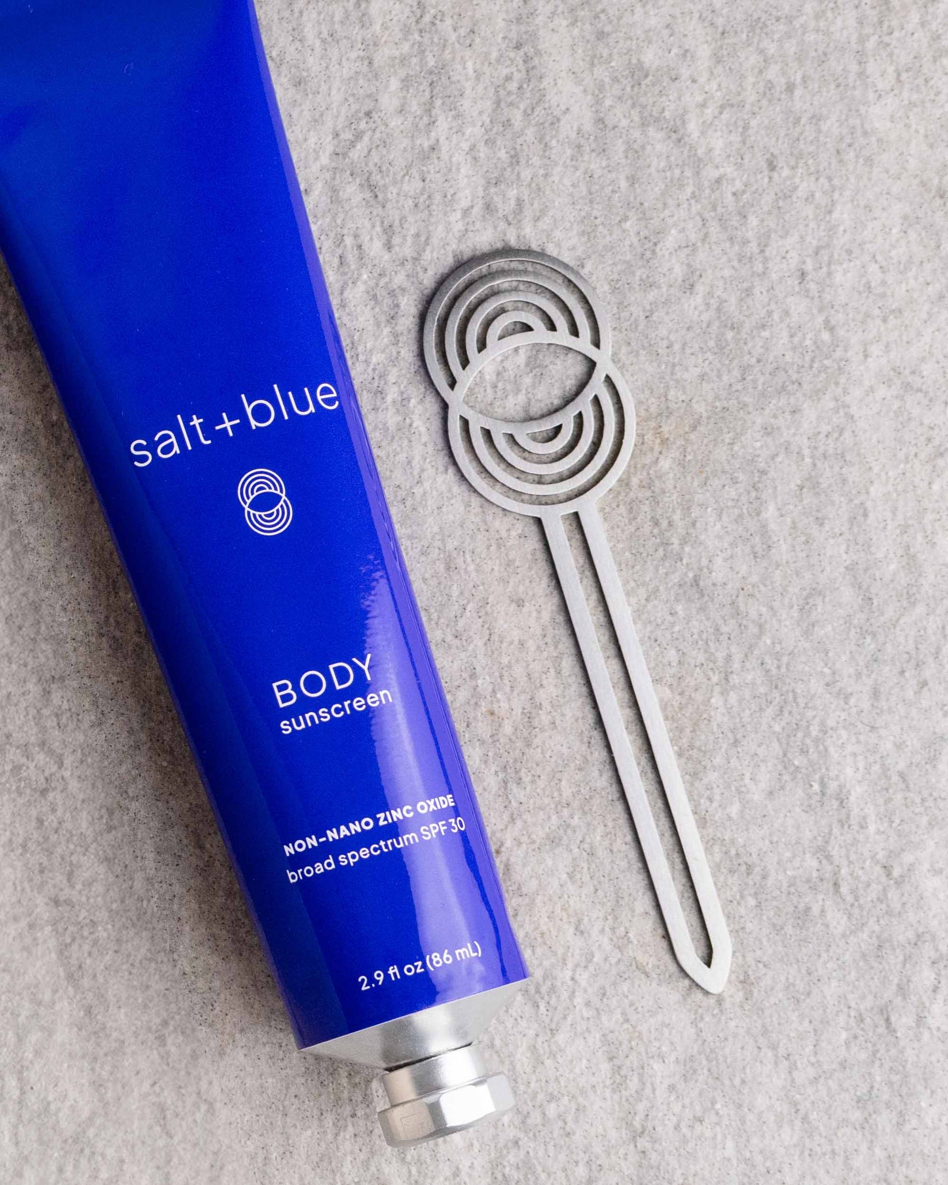Blue tube of salt+blue body sunscreen on a gray stone surface with a stainless steel tube key