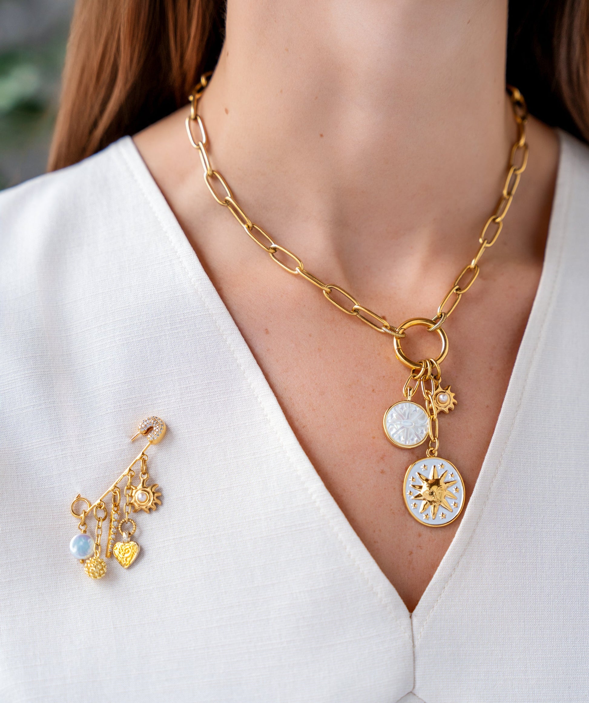 Gold celestial brooch pin with dangling pearl, crystal pavé charm, heart pendant, textured orb, and sunburst charm.