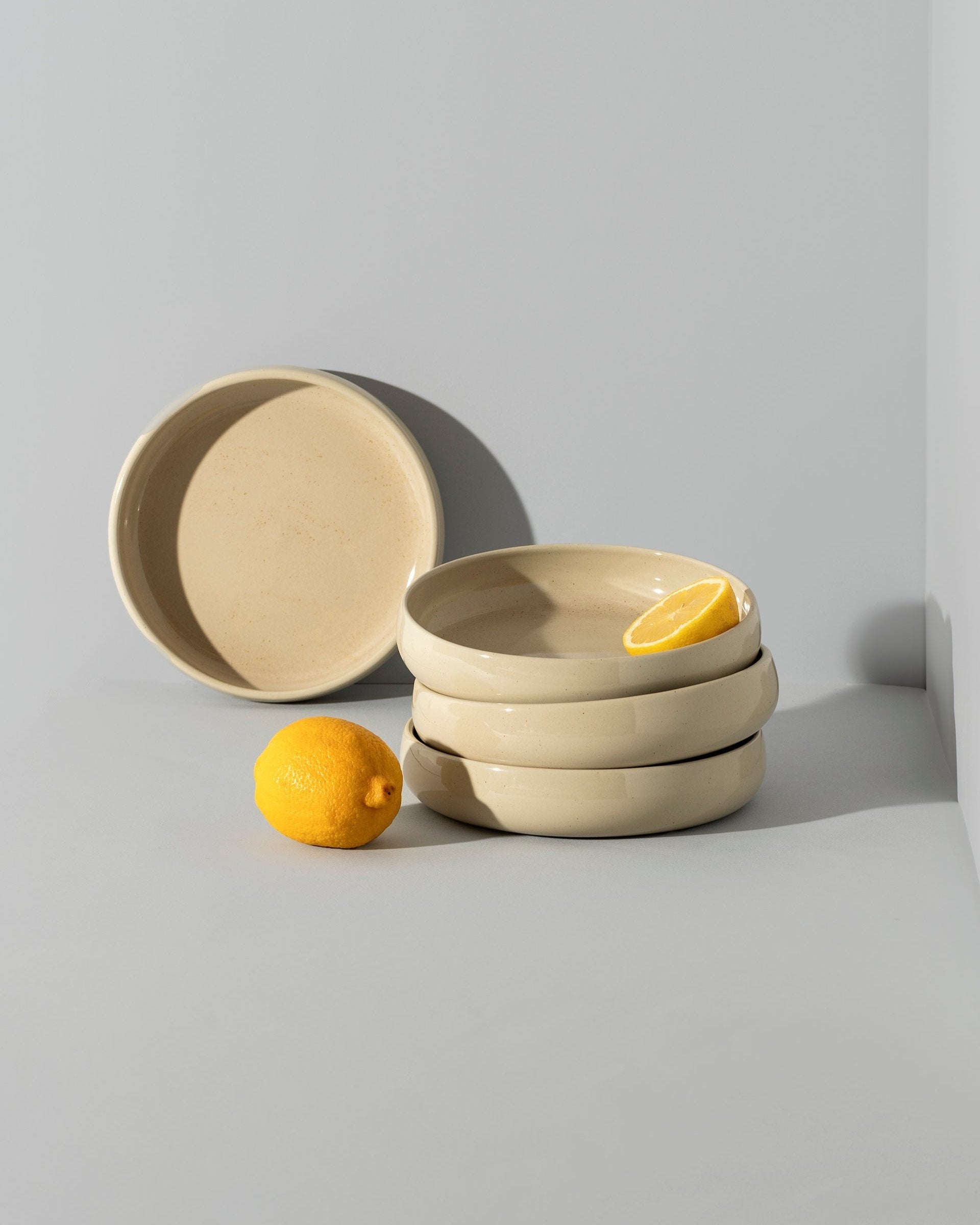 A beige stoneware pasta/salad plate with a contemporary round shape, displayed in a stacked arrangement with a white vegetable on the side.