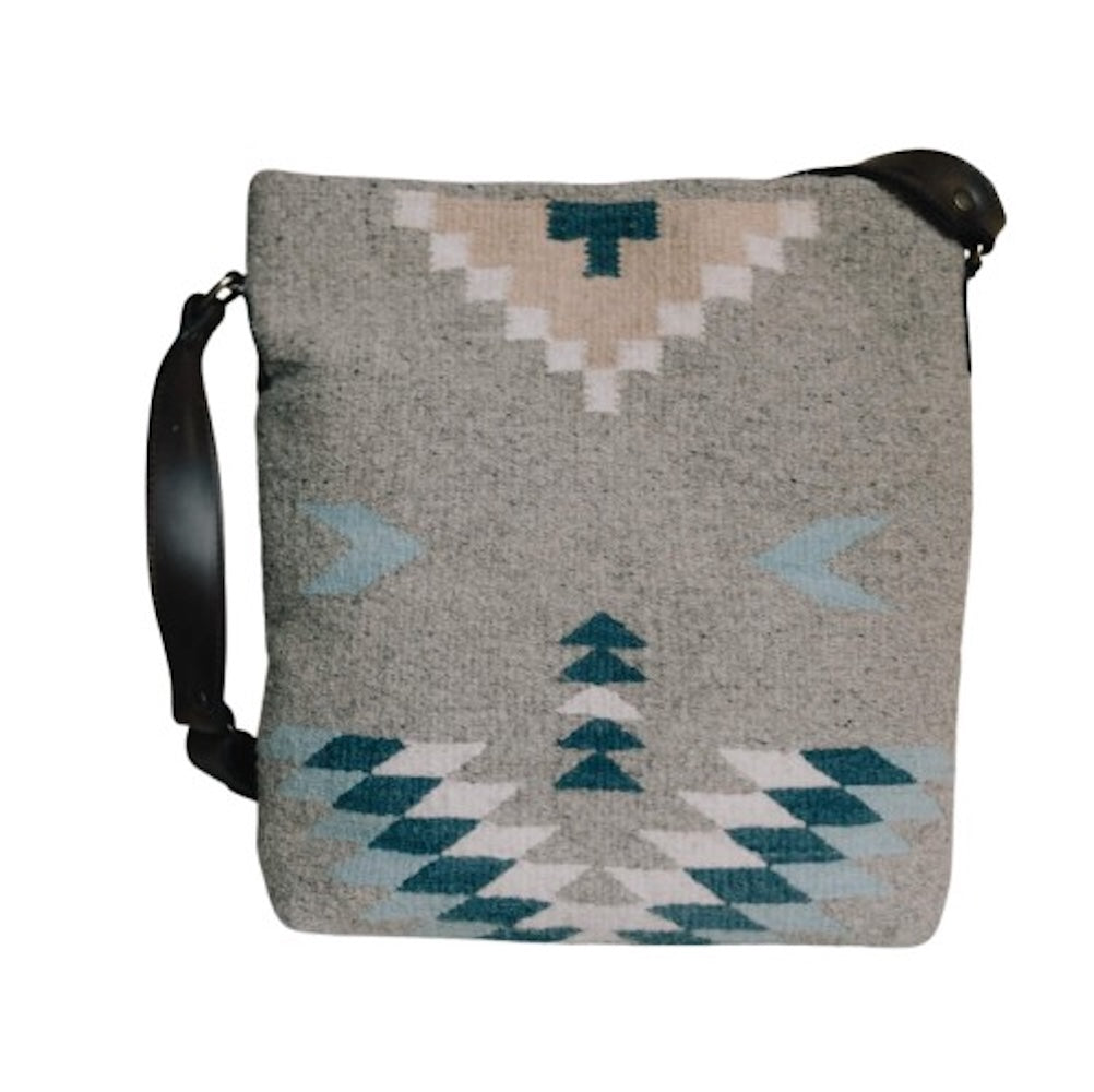 Woman with an AMASOUK handwoven wool Aguila Shoulder/Crossbody bag showcasing a Zapotec pattern in blue, ivory, and honey on a gray backdrop. Perfect for everyday activities and evening events.
