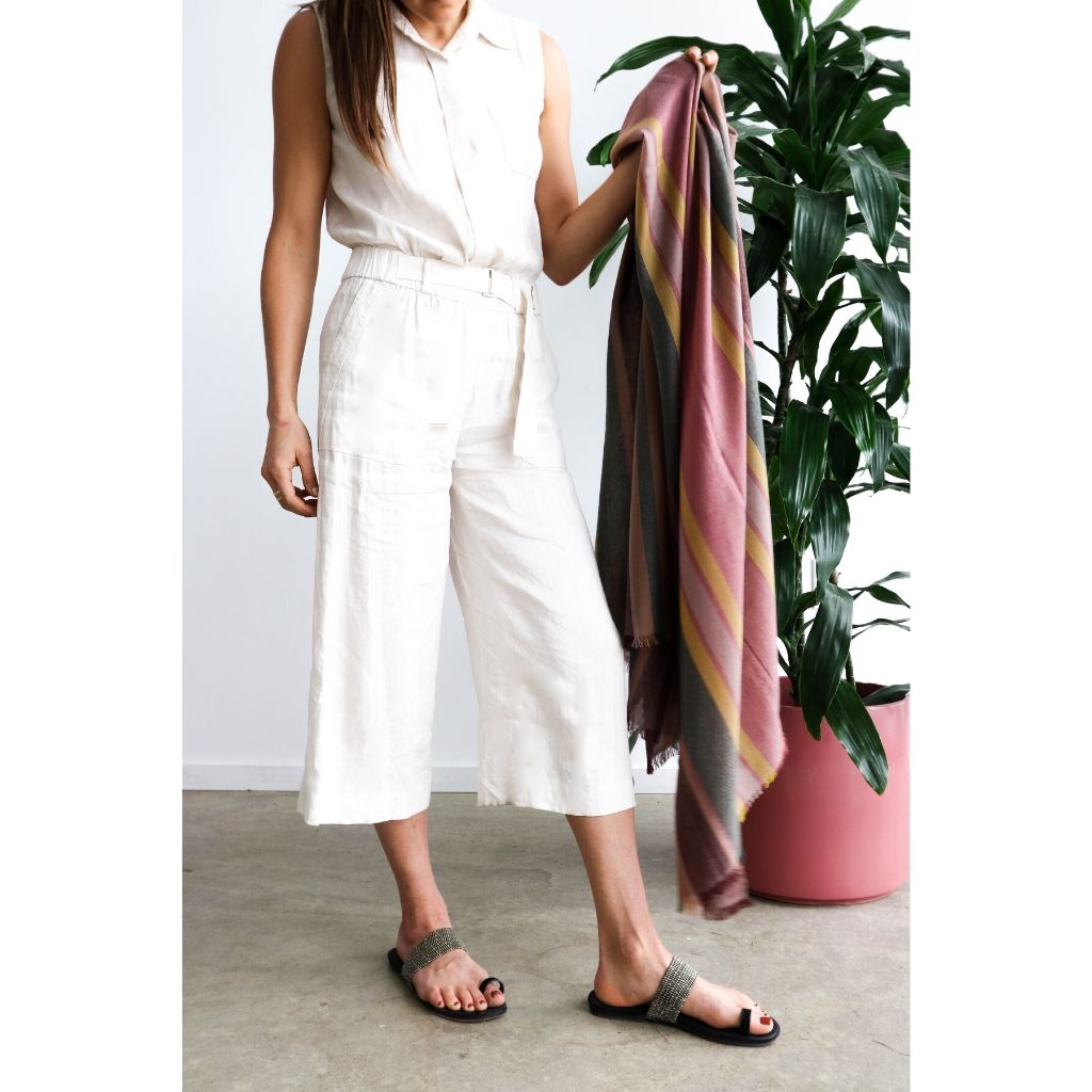 Woman in a light outfit holding Barque Clay Modern Artisan Striped Soft Merino Handwoven Scarf next to a plant.