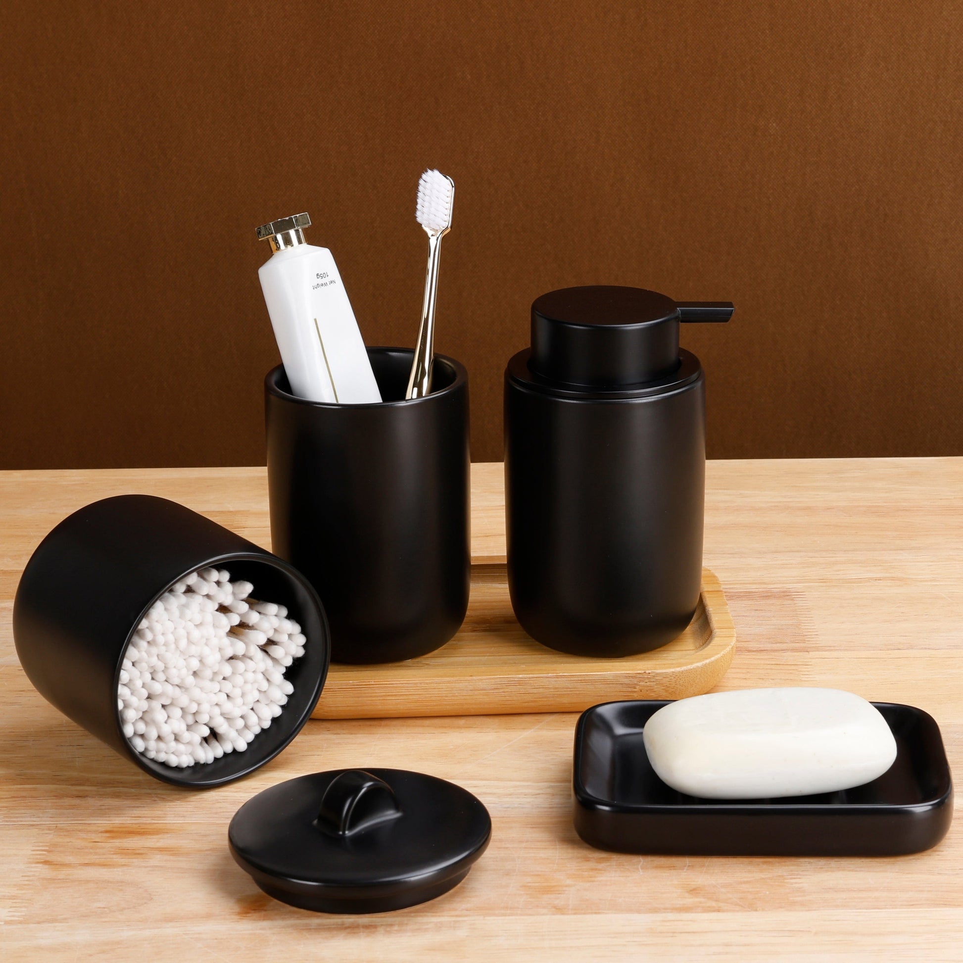 Black bathroom accessories including a container with toothbrushes, a soap dispenser, and a soap dish on a wooden surface.