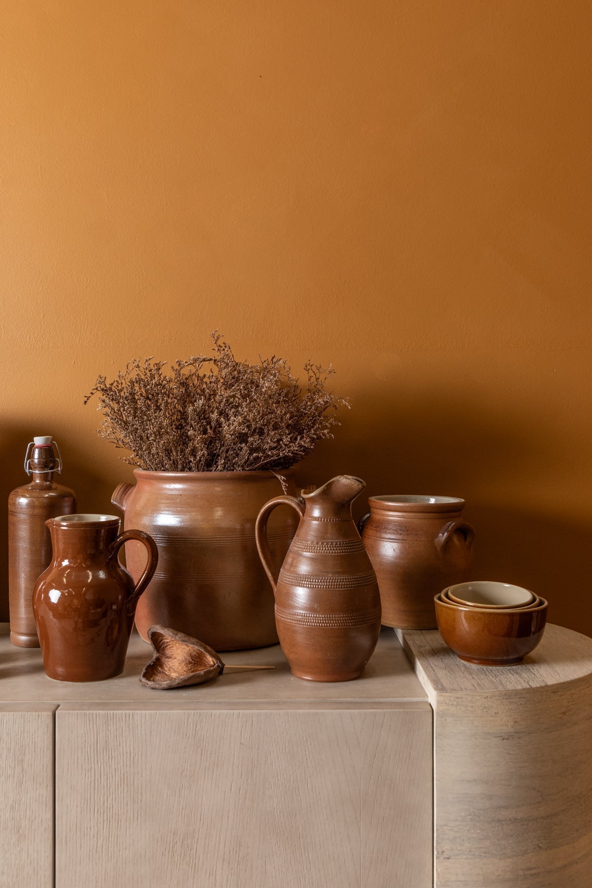 Collection of brown ceramic pots and a vase on a wooden surface against an orange wall.