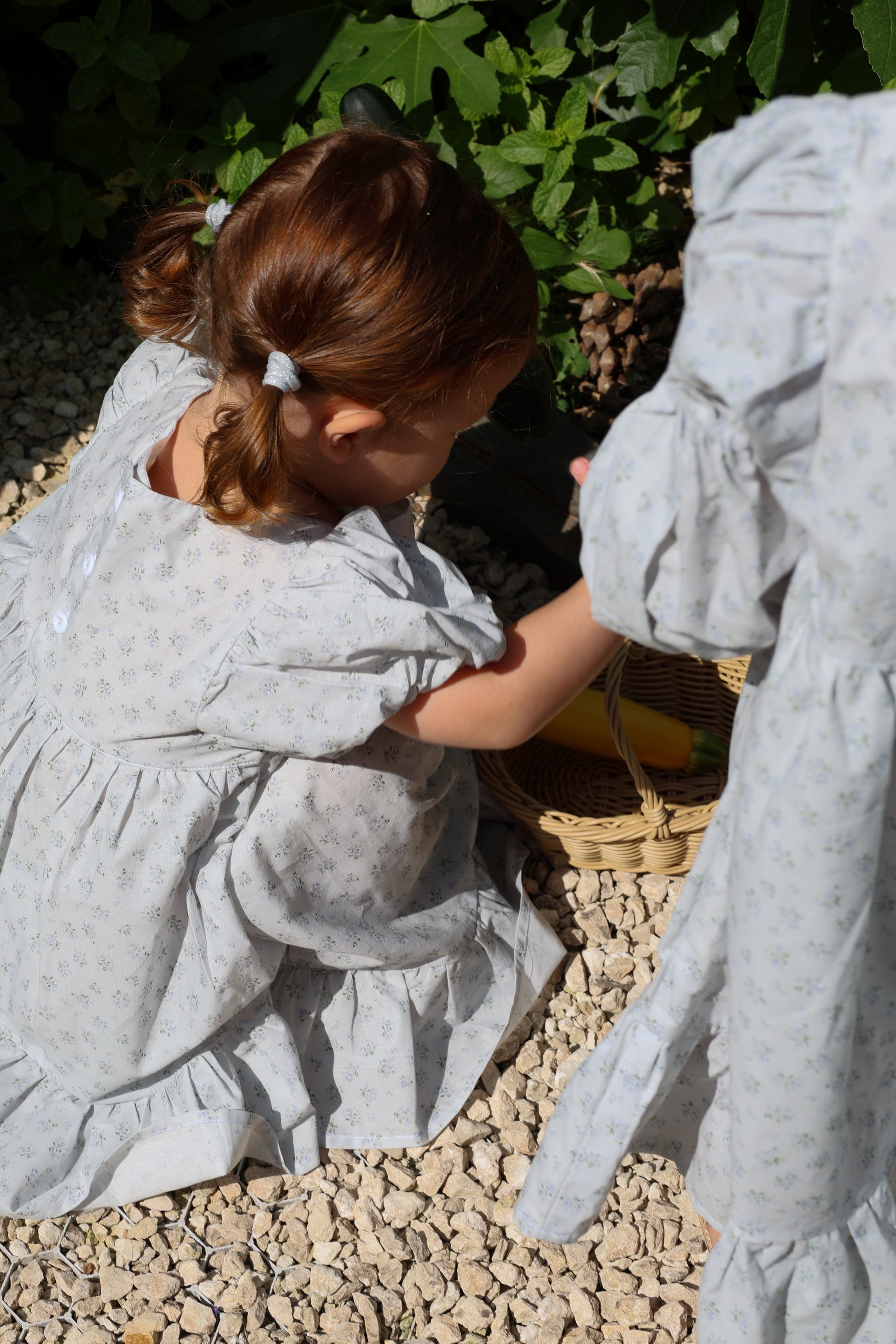 Child in a light gray dress interacting with a stone statue outdoors.