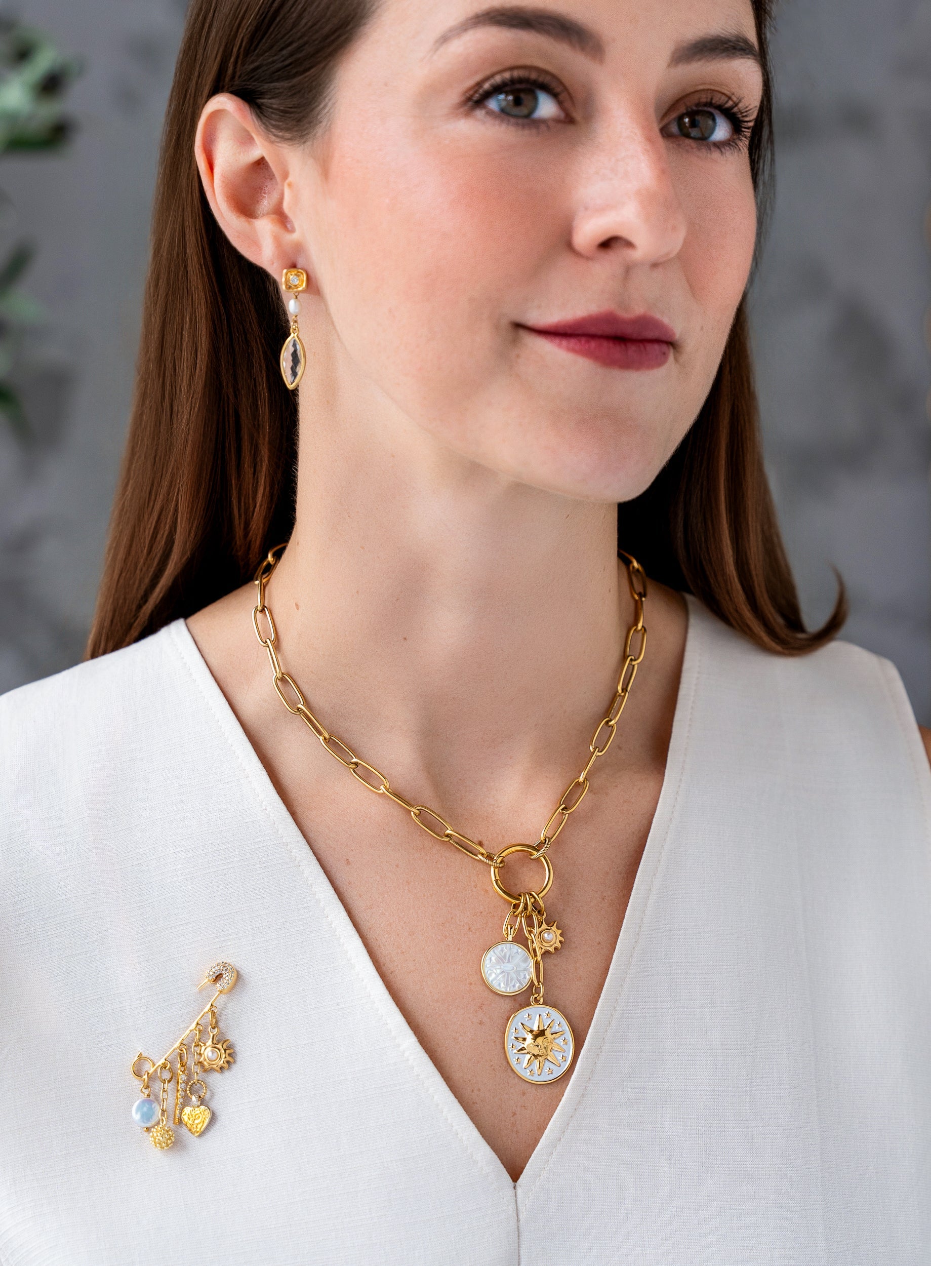 Gold celestial brooch pin with dangling pearl, crystal pavé charm, heart pendant, textured orb, and sunburst charm.