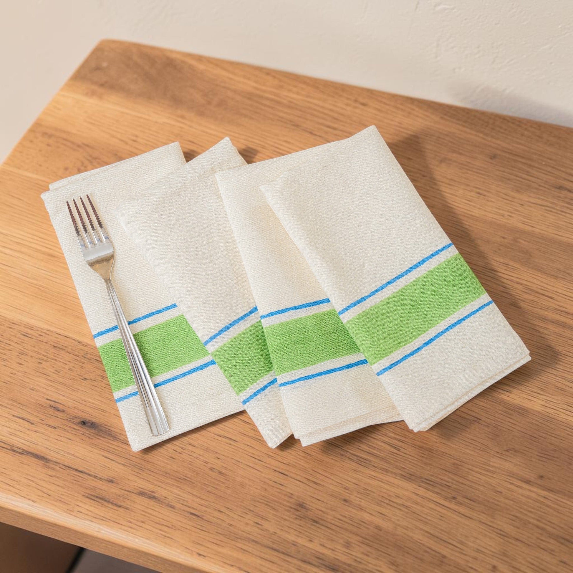Set of four white napkins with green and blue stripes hand block printed linen, on a wooden surface.