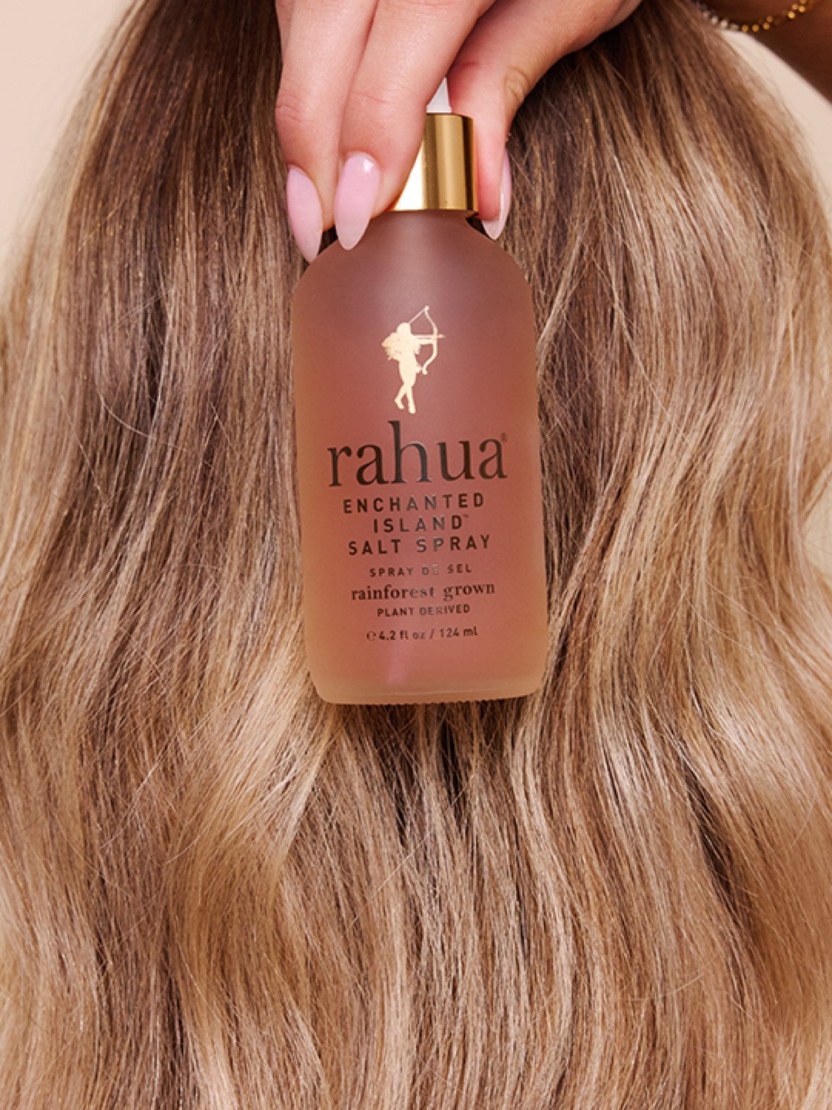 model holding enchanted island salt spray in front of wavy blonde hair