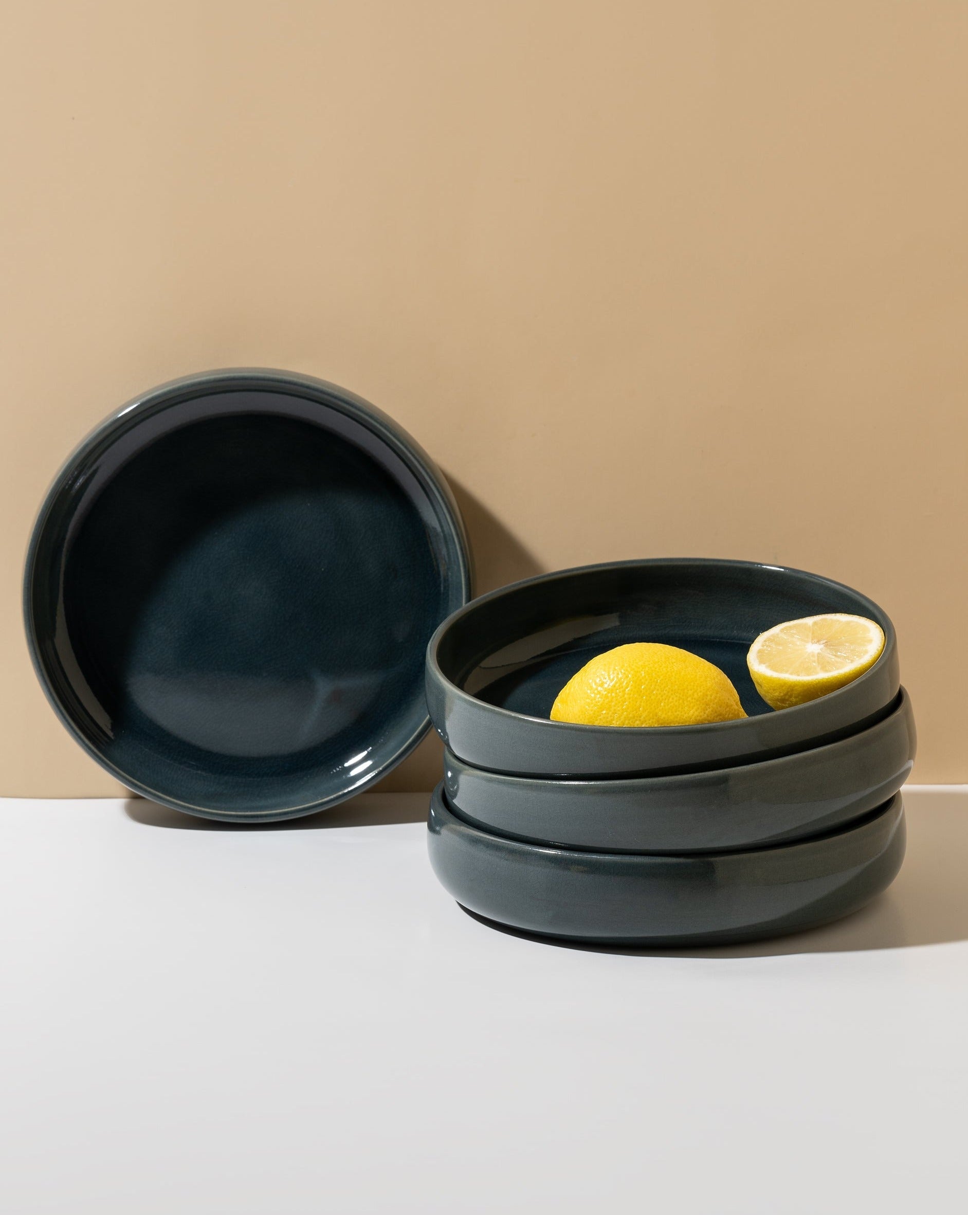 A beige stoneware pasta/salad plate with a contemporary round shape, displayed in a stacked arrangement with a white vegetable on the side.
