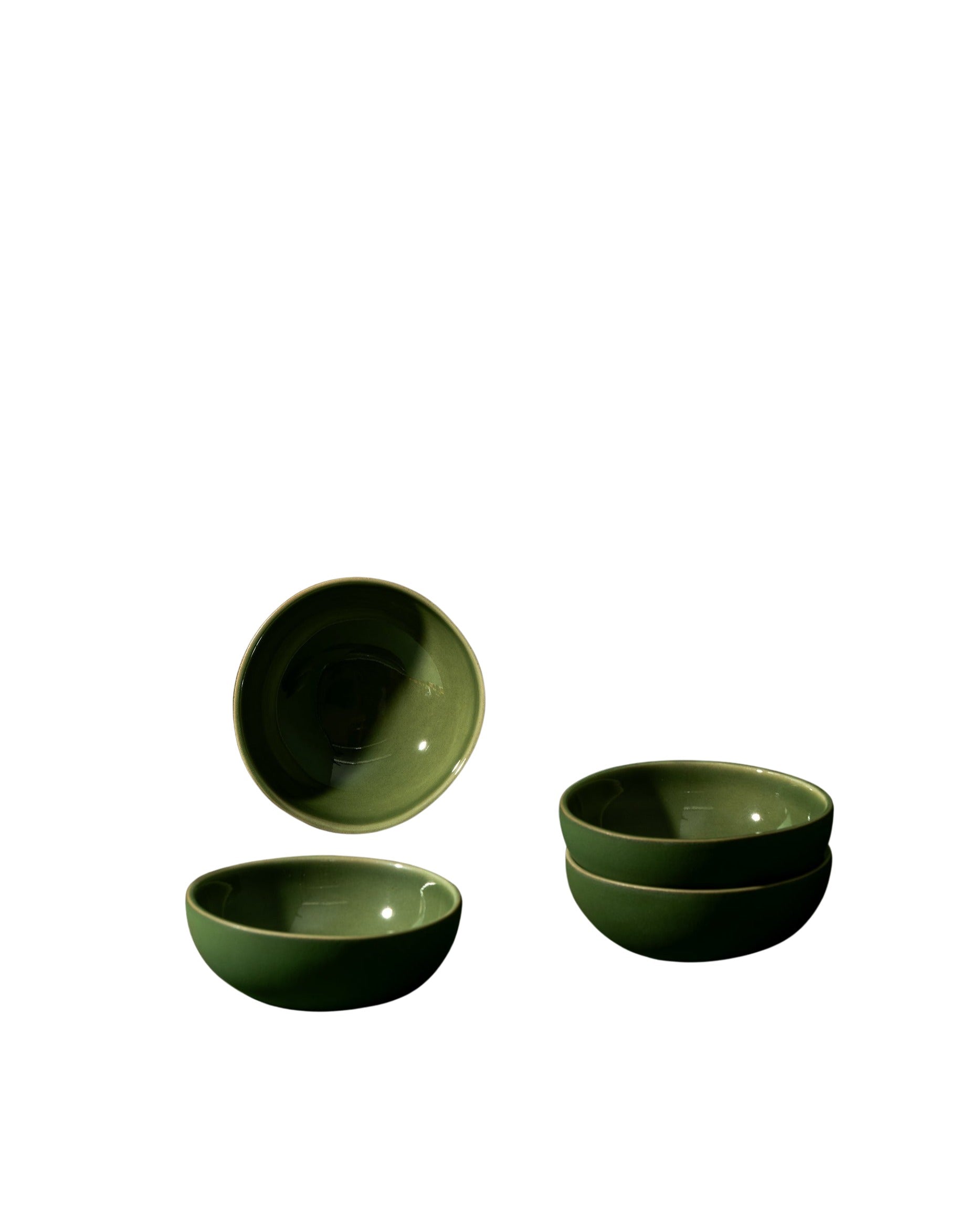 A set of white stoneware condiment bowls with a matte finish, displayed against a neutral background. One bowl is upright, while the others are stacked behind it, and there is a small wooden spoon in front.
