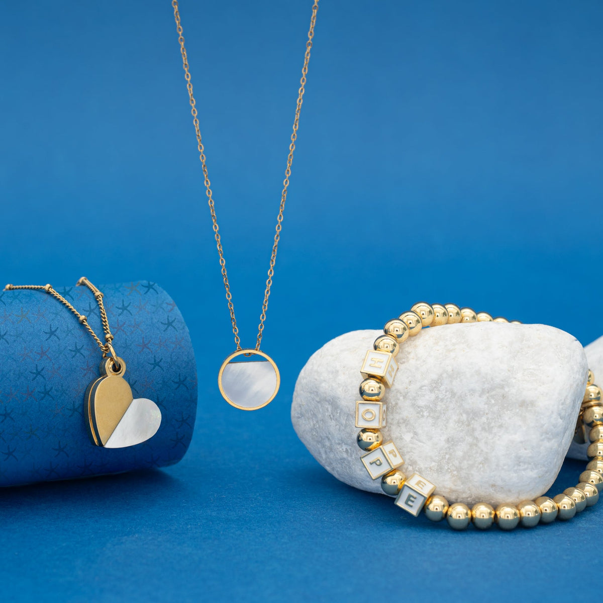 Give Hope, Wear Hope bracelet styled with a heart locket and round pendant necklace on blue