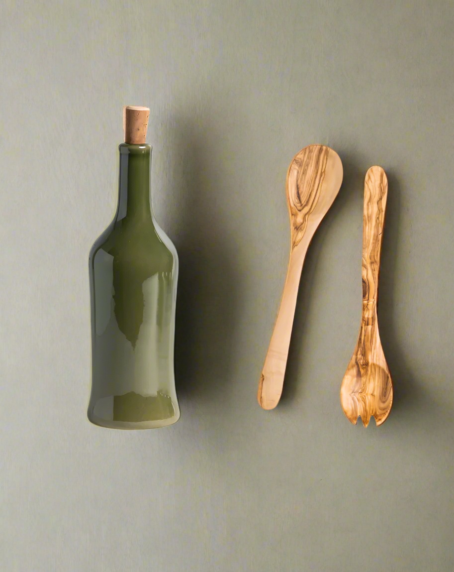 A handcrafted olive wood salad server set accompanied by a stoneware bottle, both displayed against a neutral background.