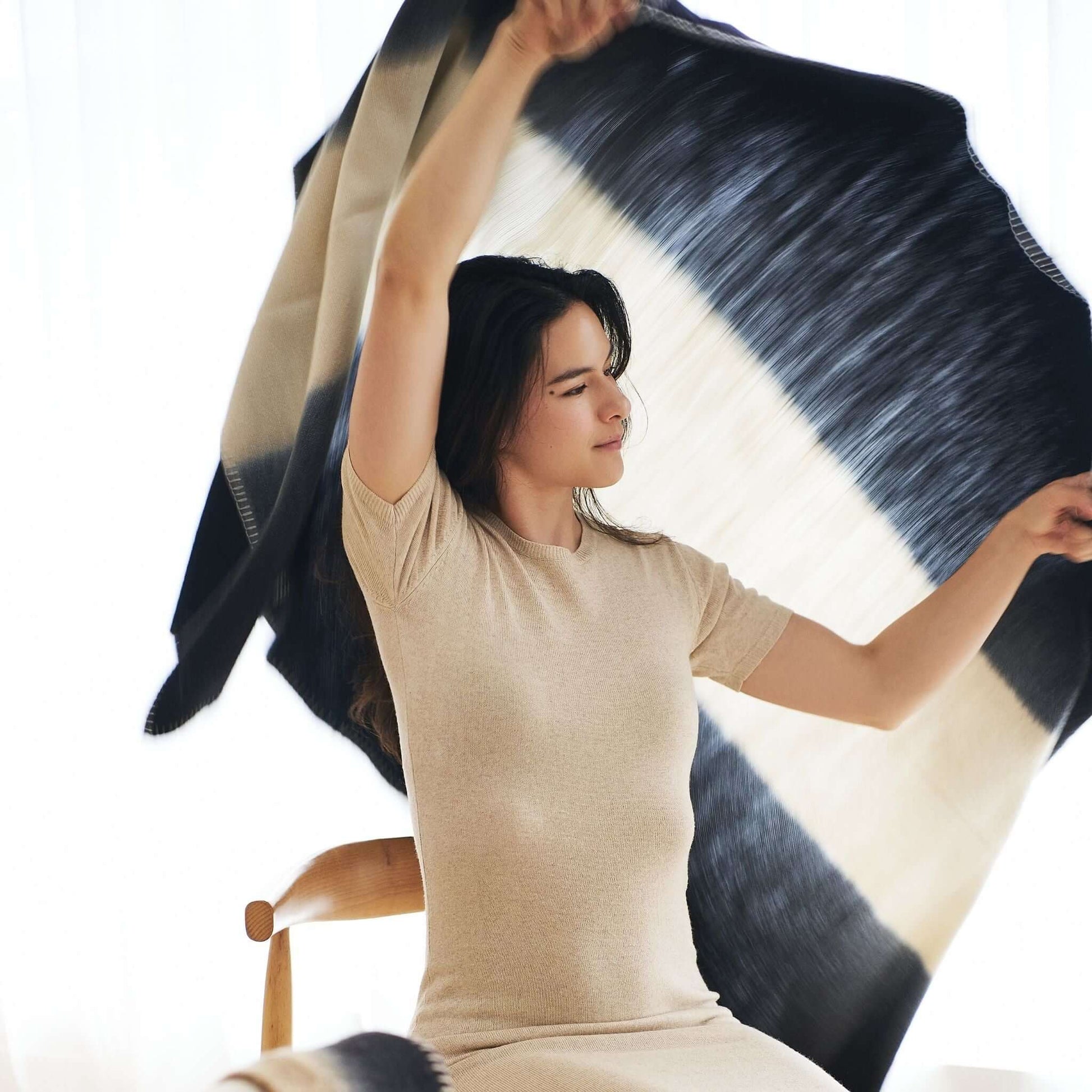 Woman joyfully displaying the Ink Black White Ombre Textured Throw In Hand Spun Merino And Hand Stitched Hem.