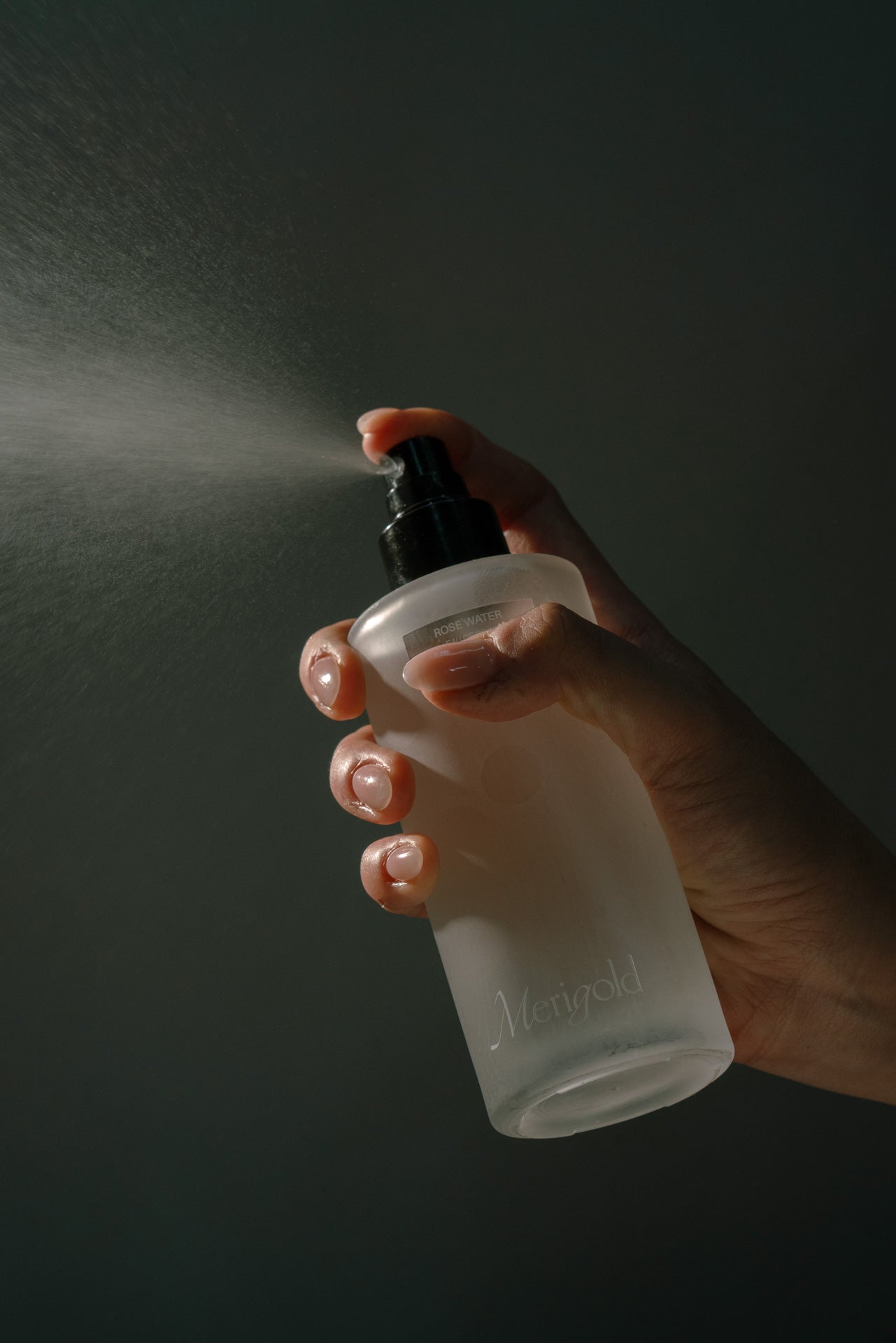 Hand holding a spray bottle with a dark background