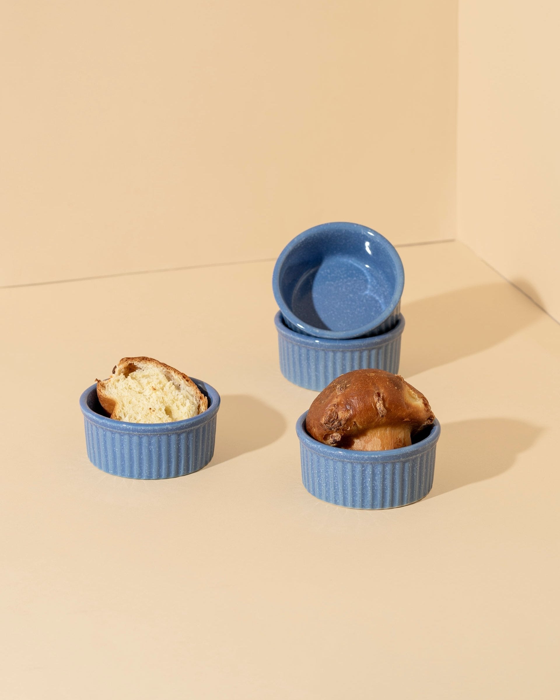 Three stoneware ramekins of varying sizes with lids, displayed on a neutral background. One ramekin contains a baked dessert, possibly a soufflé, and the other two are empty.