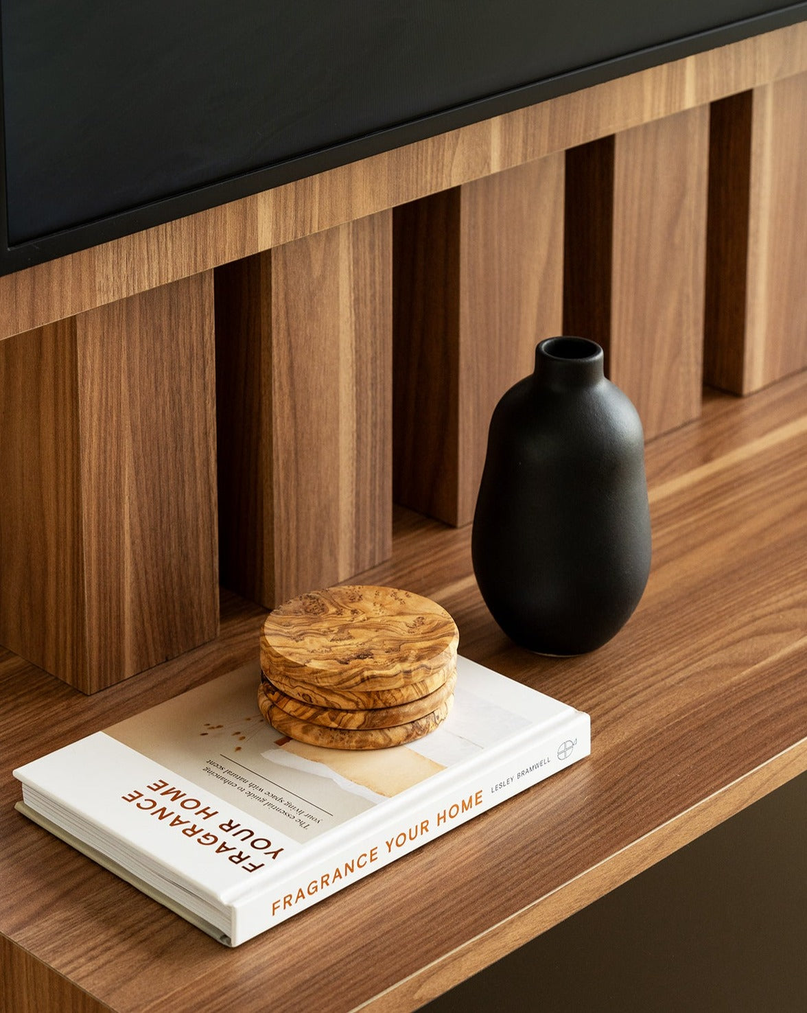 Matte black handmade stoneware vase with a minimalistic design, placed on a wooden table. Next to it is a set of four Natural Olive Wood Round Coasters stacked on top of a closed book.