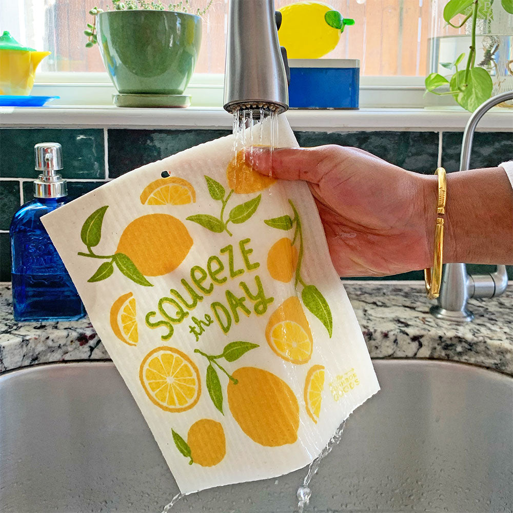 A lemon sponge cloth becomes wet under running kitchen faucet.