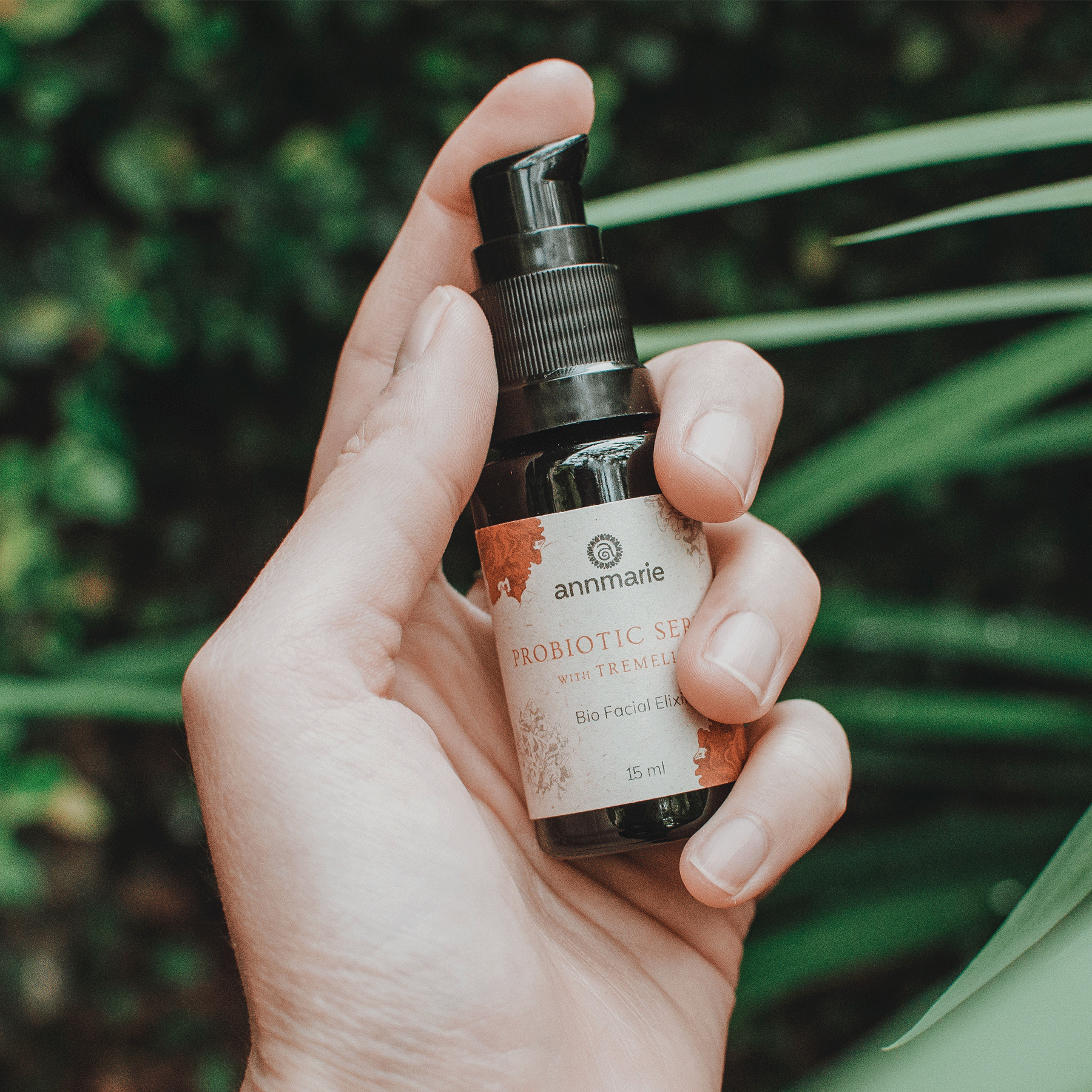 Hand holding a bottle of 'annmarie' probiotic serum with green leaves in the background