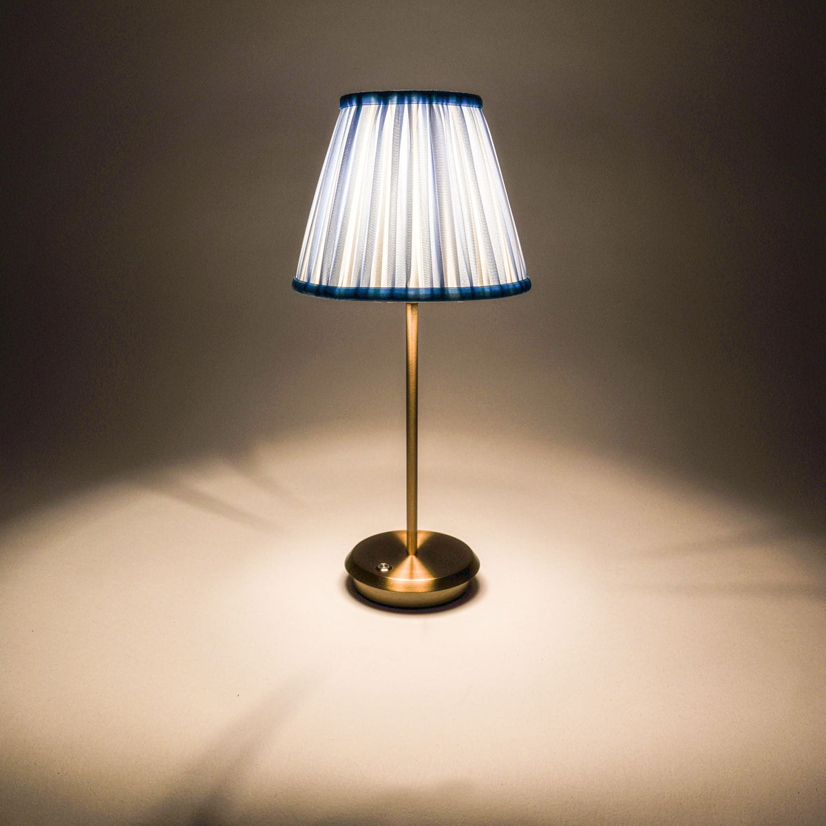 Blue Velvet Tides cordless table lamp with blue striped shade and gold base illuminated.