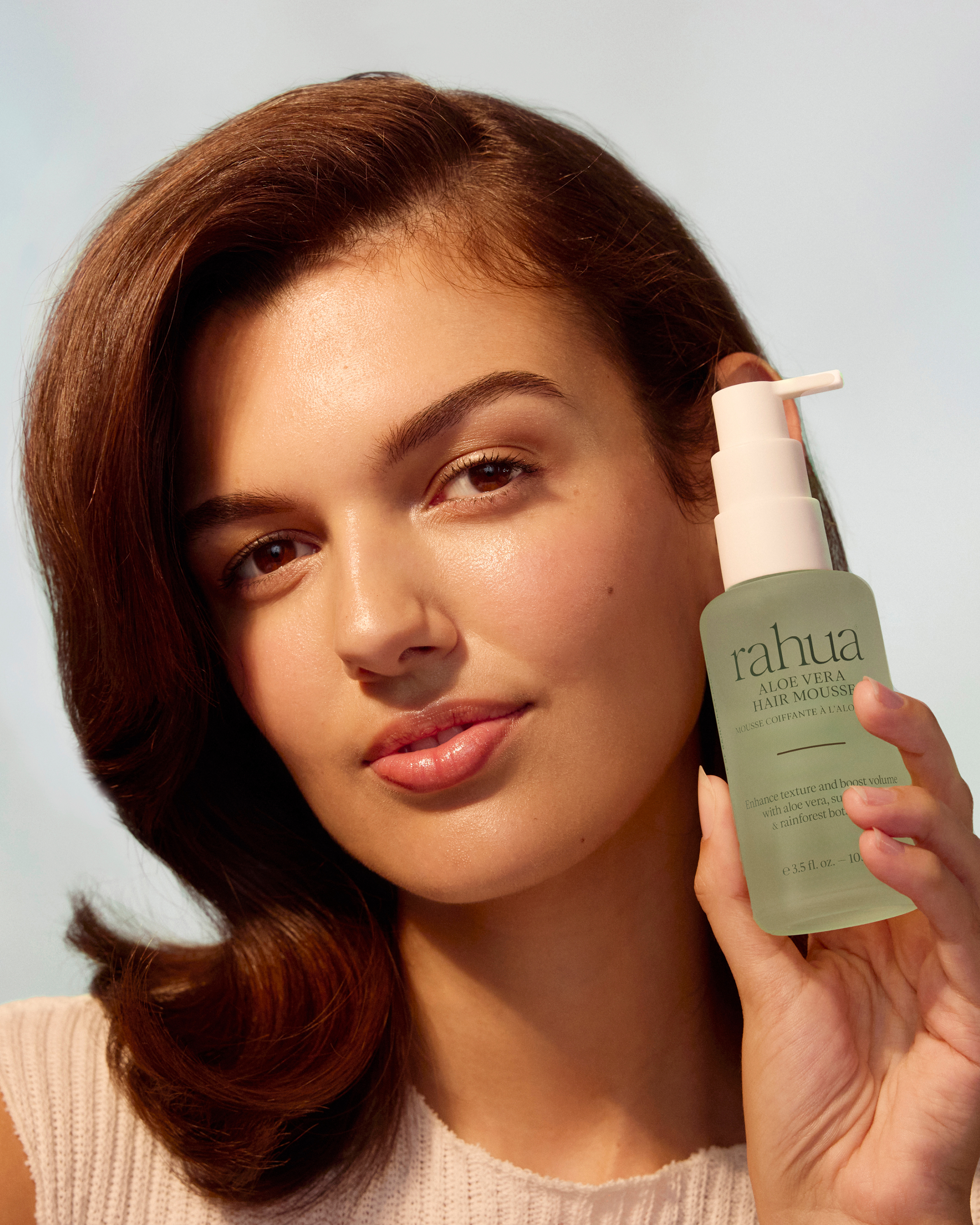 Woman holding a bottle of rahua skincare product against a neutral background