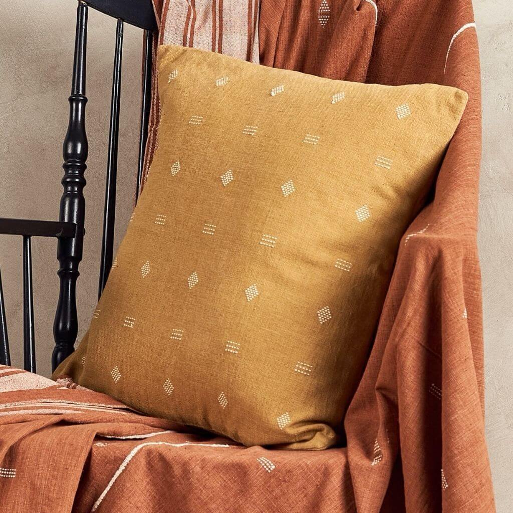 Nira Ochre Hand Spun Organic Cotton Handloom Pillow beautifully displayed on a chair with rich earthy tones.