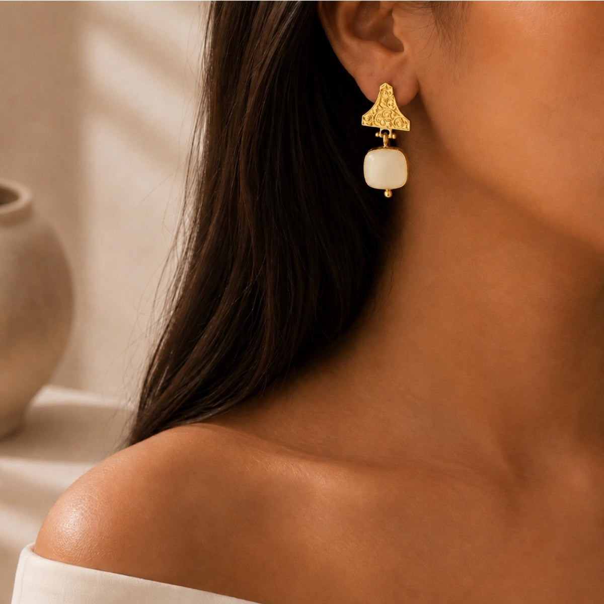 close-up of a woman wearing a gold dangle white snow Quartz gemstone earring with a, shown against a warm neutral background
