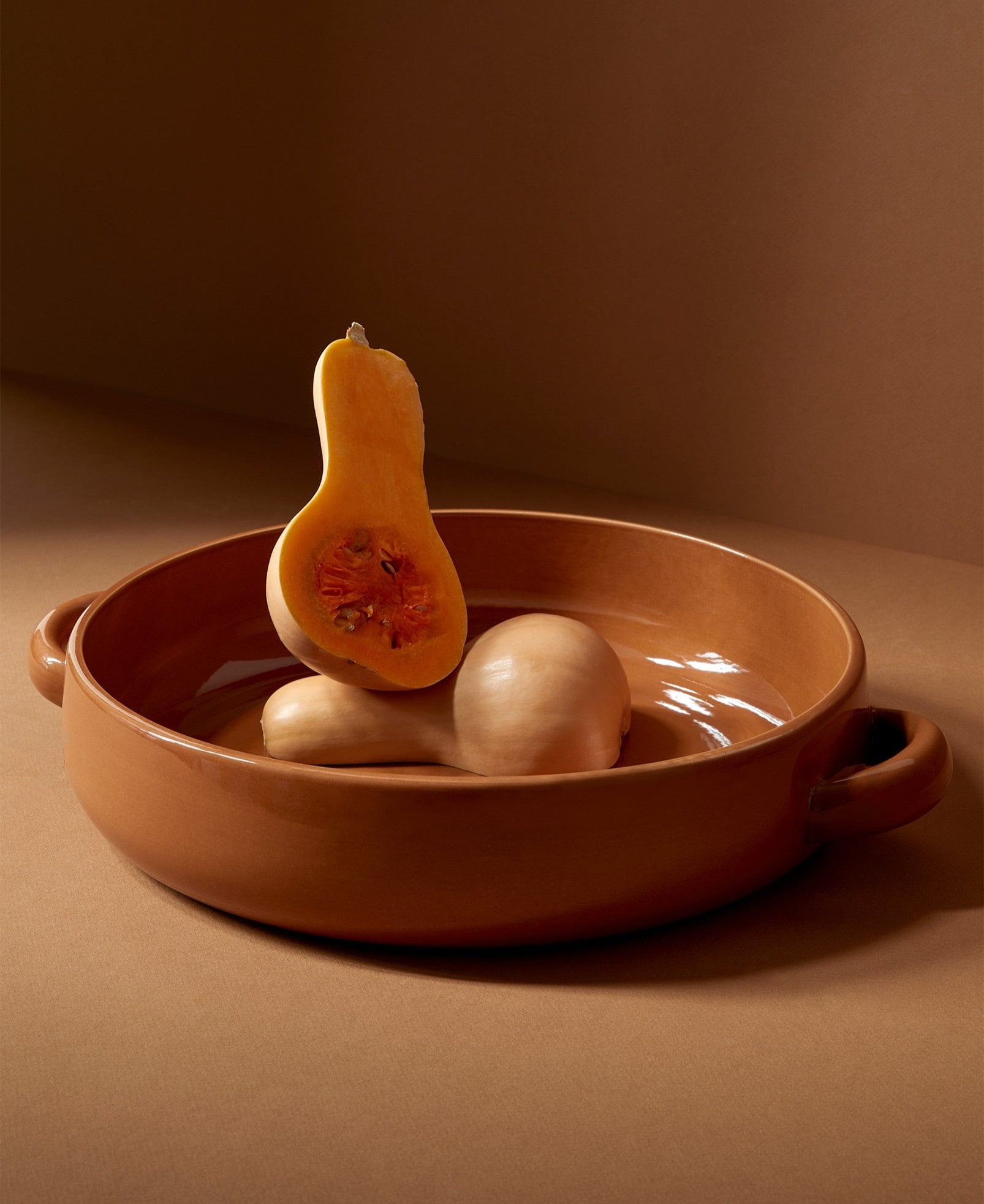A beige stoneware serving platter with handles, containing what appears to be a roasted vegetable, placed on a brown surface.