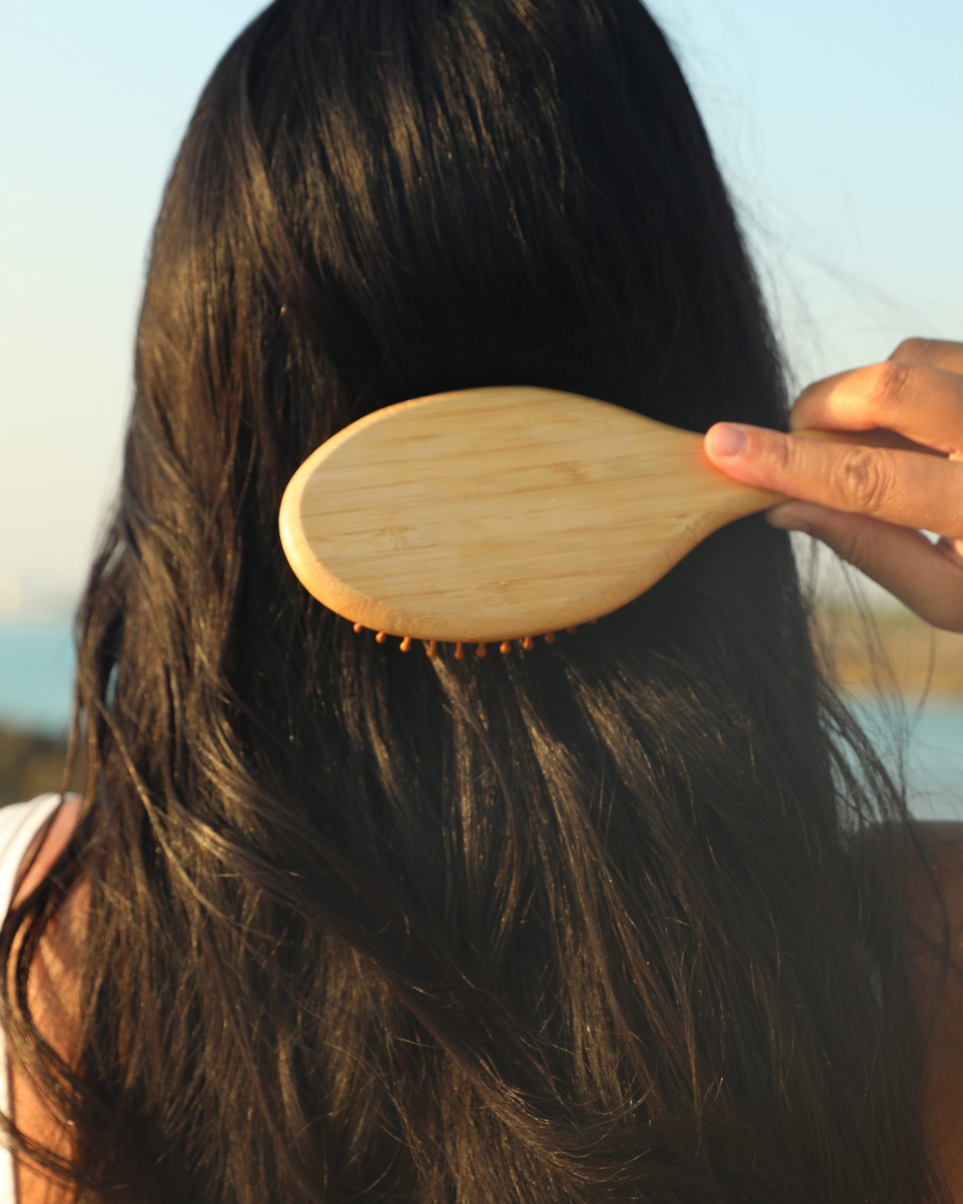 Person using a wooden hairbrush on their long hair with a blurred natural background|variant:42-oz
