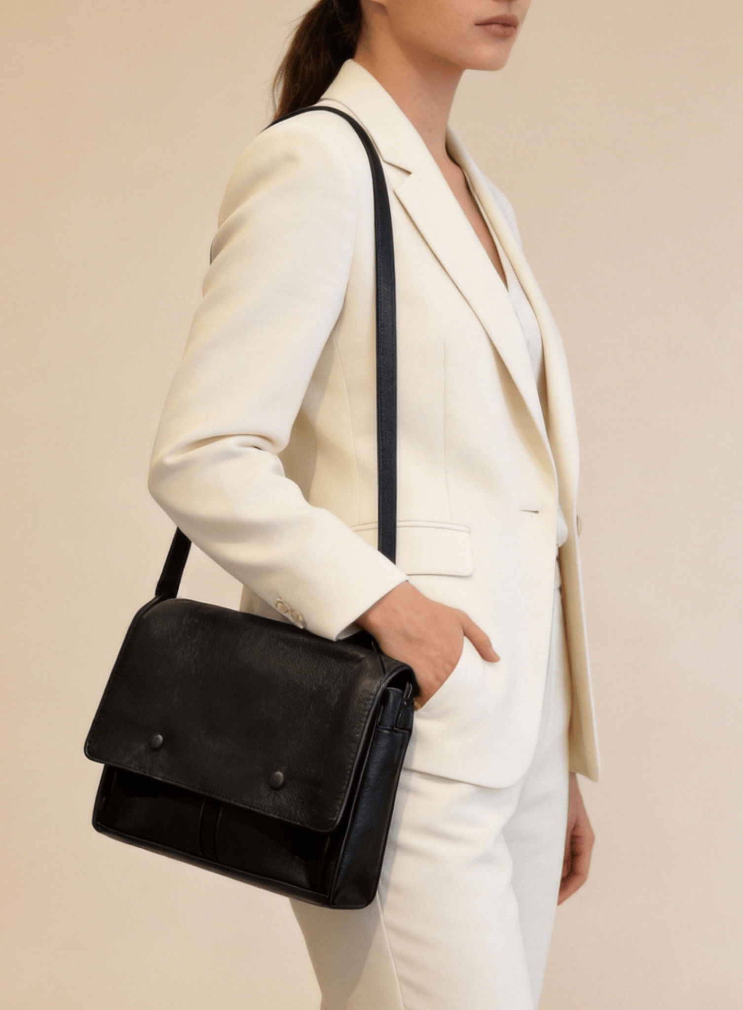 Person wearing a white suit with a black shoulder bag on a beige background