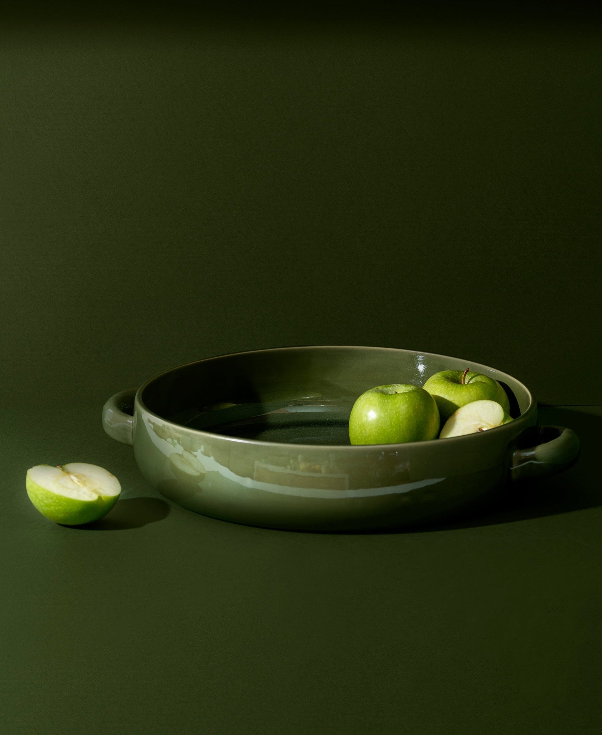 A white stoneware serving plate with handles, featuring a minimalist design, displayed with a piece of cauliflower on it, set against a neutral background.