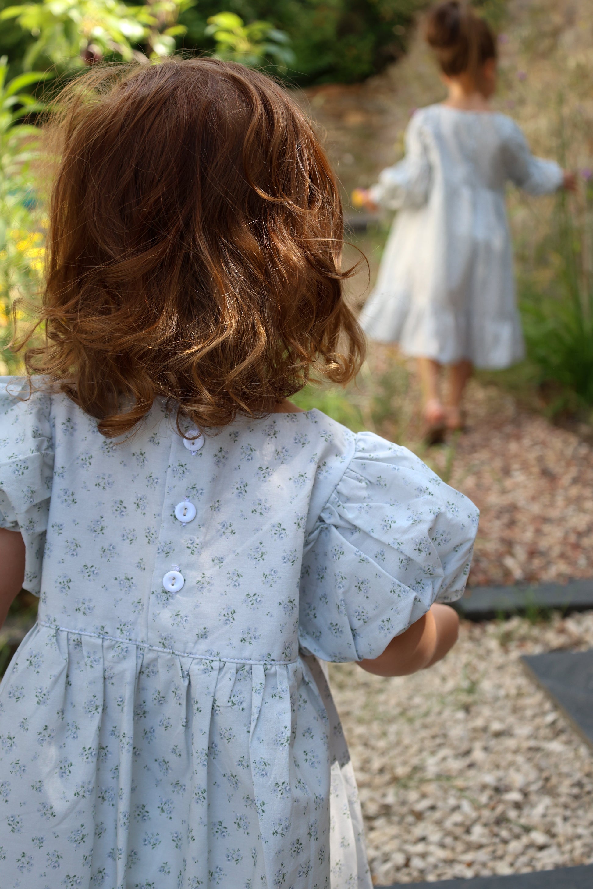 Two children in light blue dresses standing in a garden.