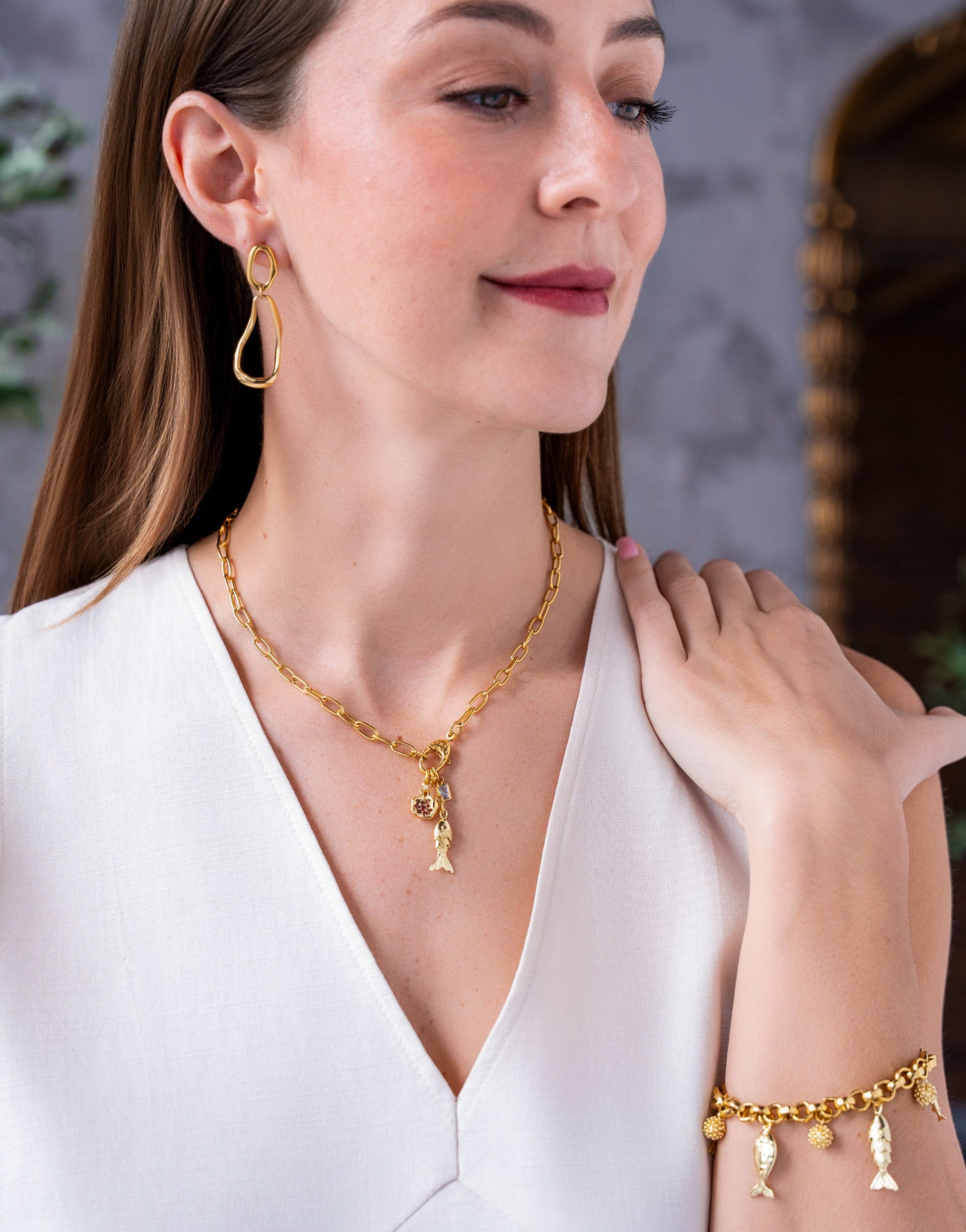 Gold charm bracelet with dangling fish charms and textured gold bead accents on a chunky chain.