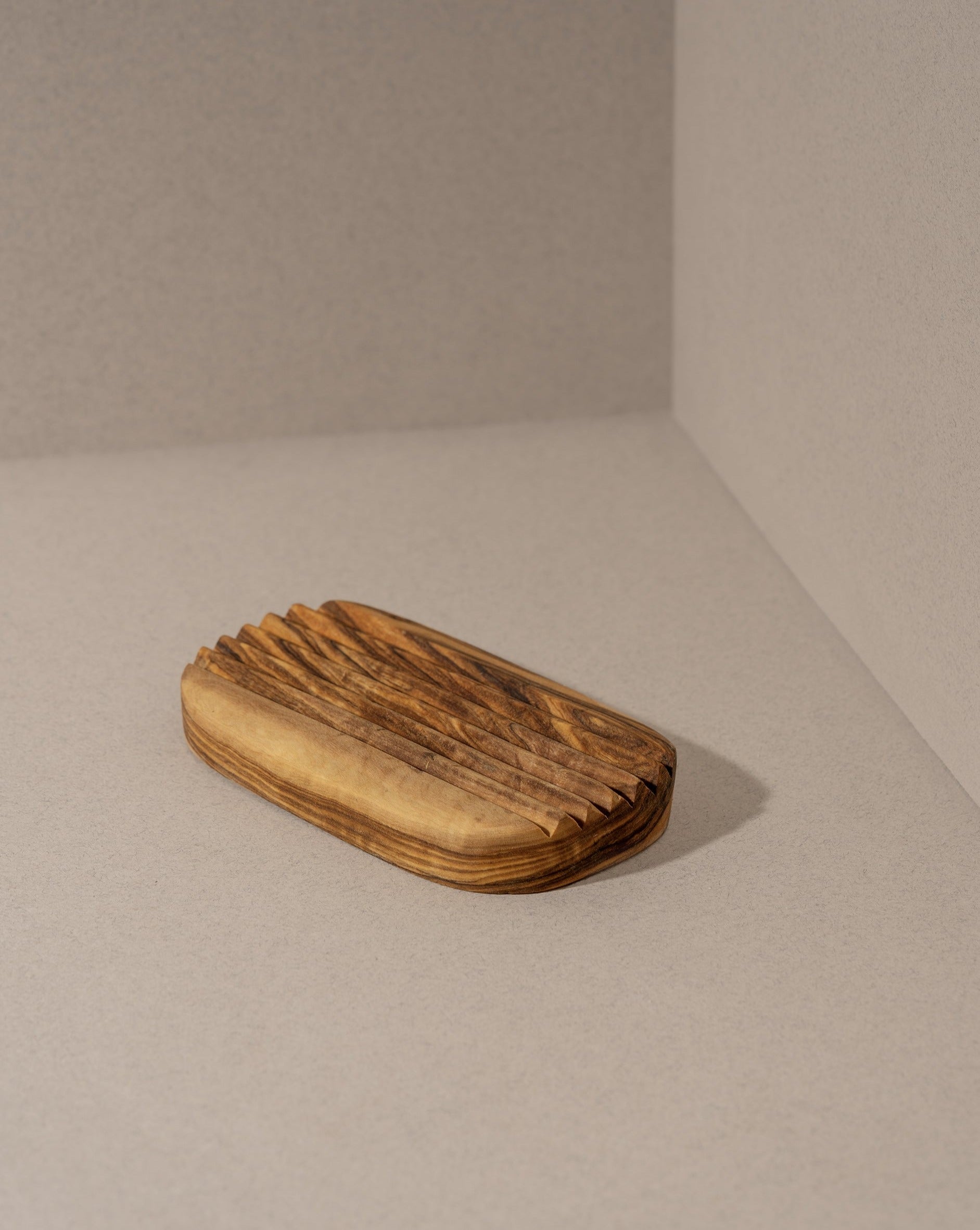 An olive wood soap holder with a natural pattern, placed on a neutral background.