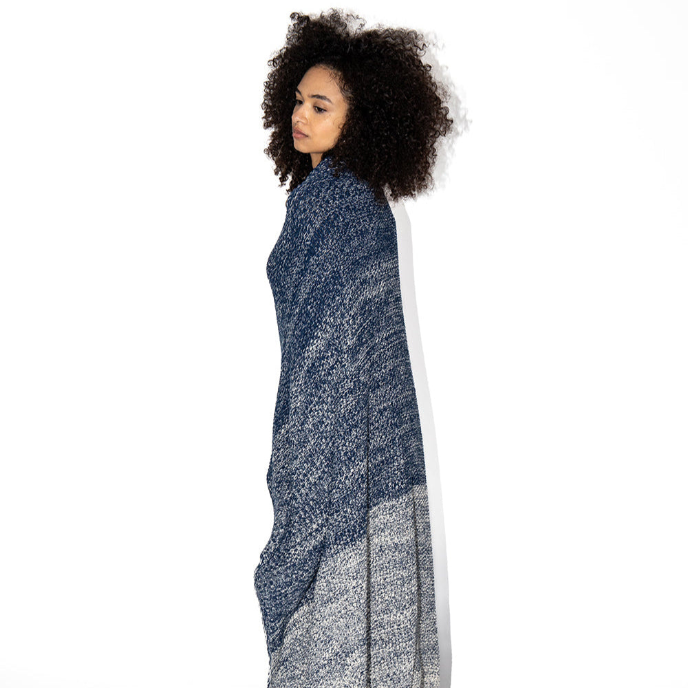 Woman wrapped in a knitted navy and grey cotton blanket with a white background.