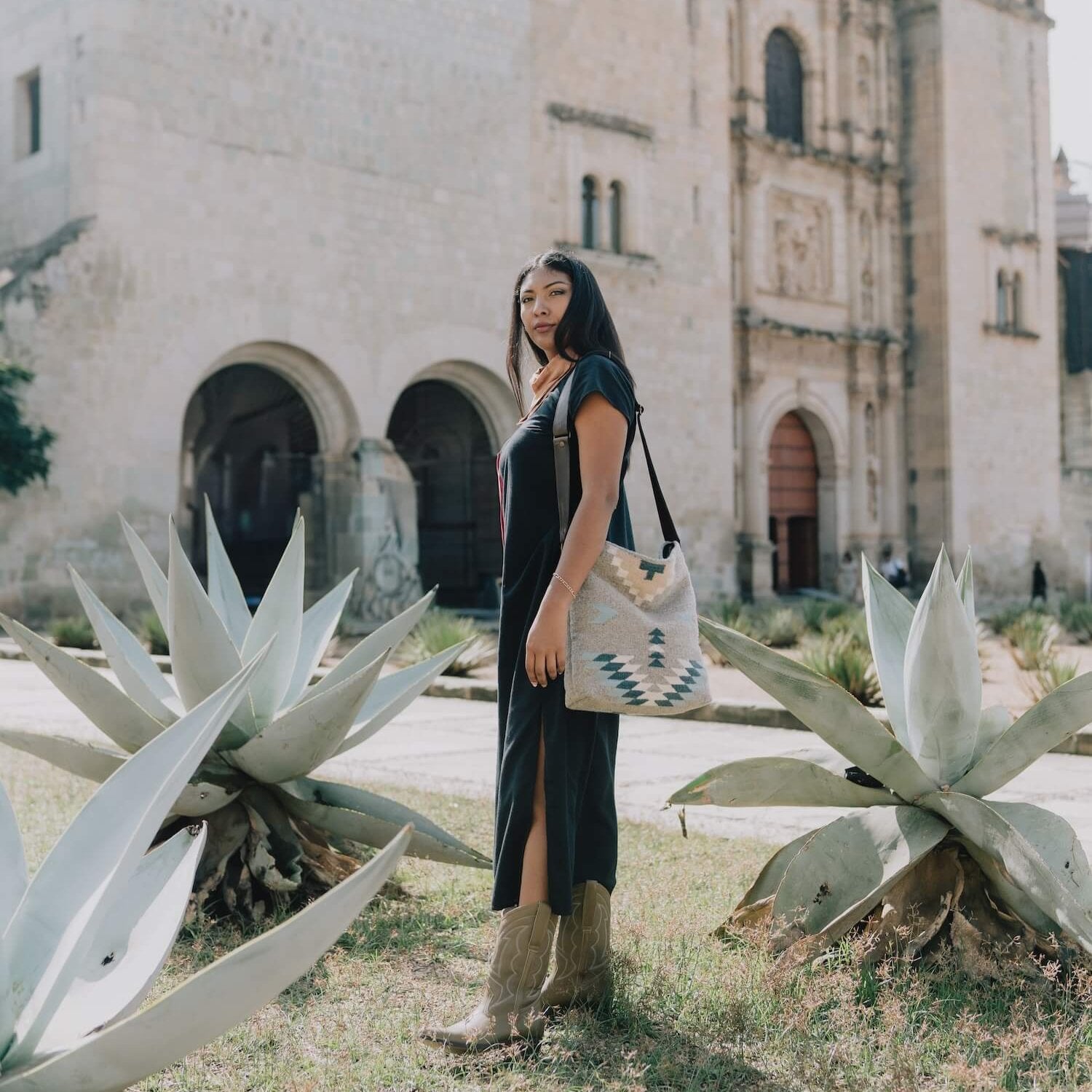 Effortlessly chic woman carrying an AMASOUK handwoven wool Aguila Shoulder/Crossbody bag with a Zapotec design in blue, ivory, and honey on a gray background. A versatile accessory for any occasion.