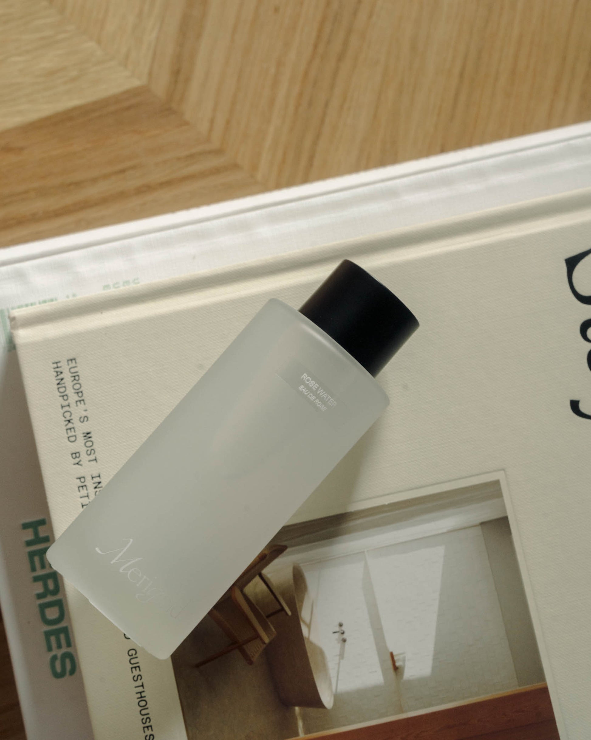 Merigold Rose Water bottle styled on neutral books and wood surface – hydrating, soothing floral toner for dry and sensitive skin. Clean, plant-based skincare.